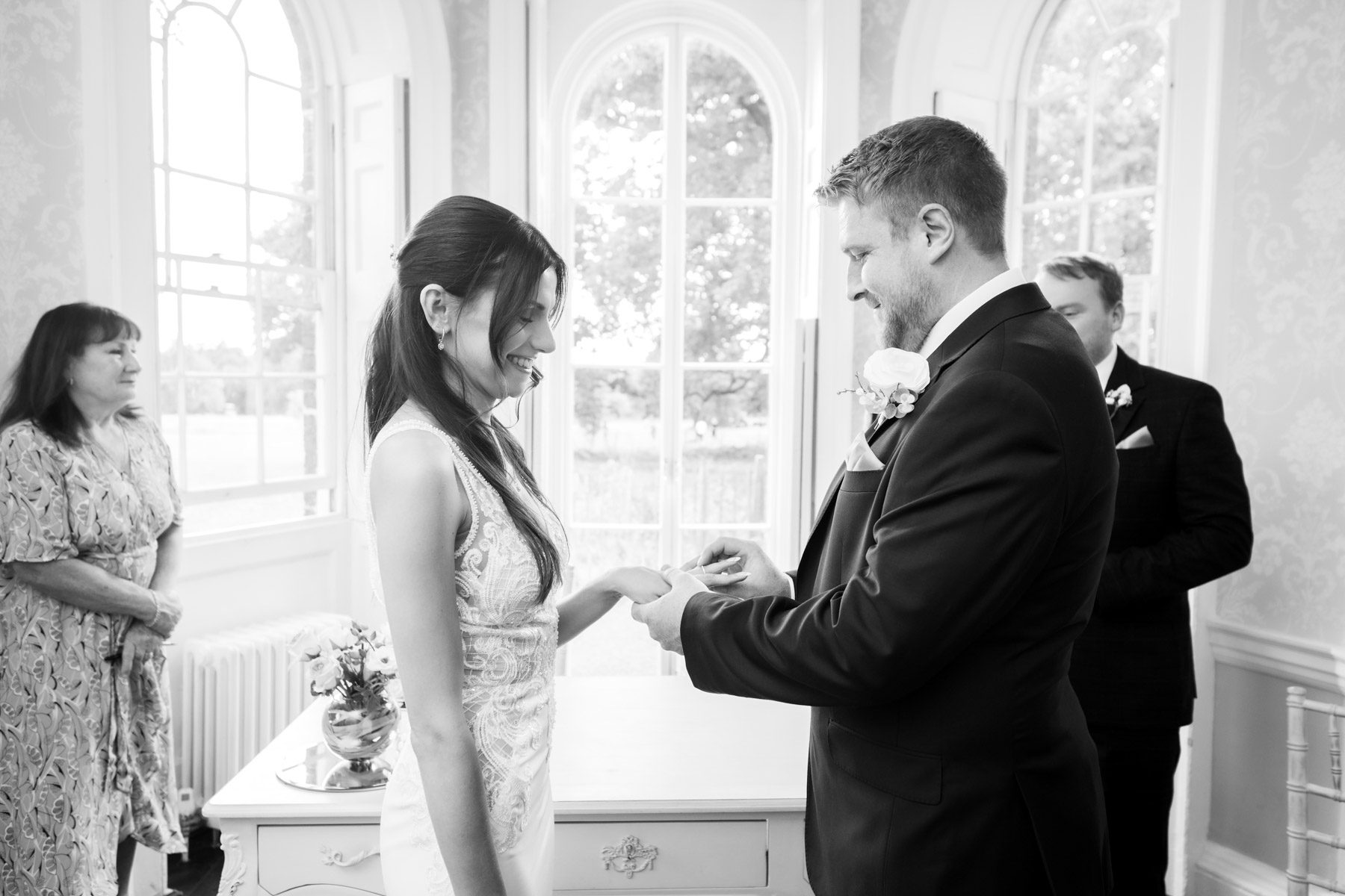 Black and white photo of groom placing the ring on bride's finger