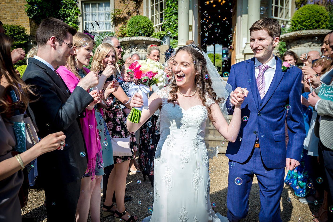 Bride and Groom laughing as bubbles are blown as they leave Hampton Court House