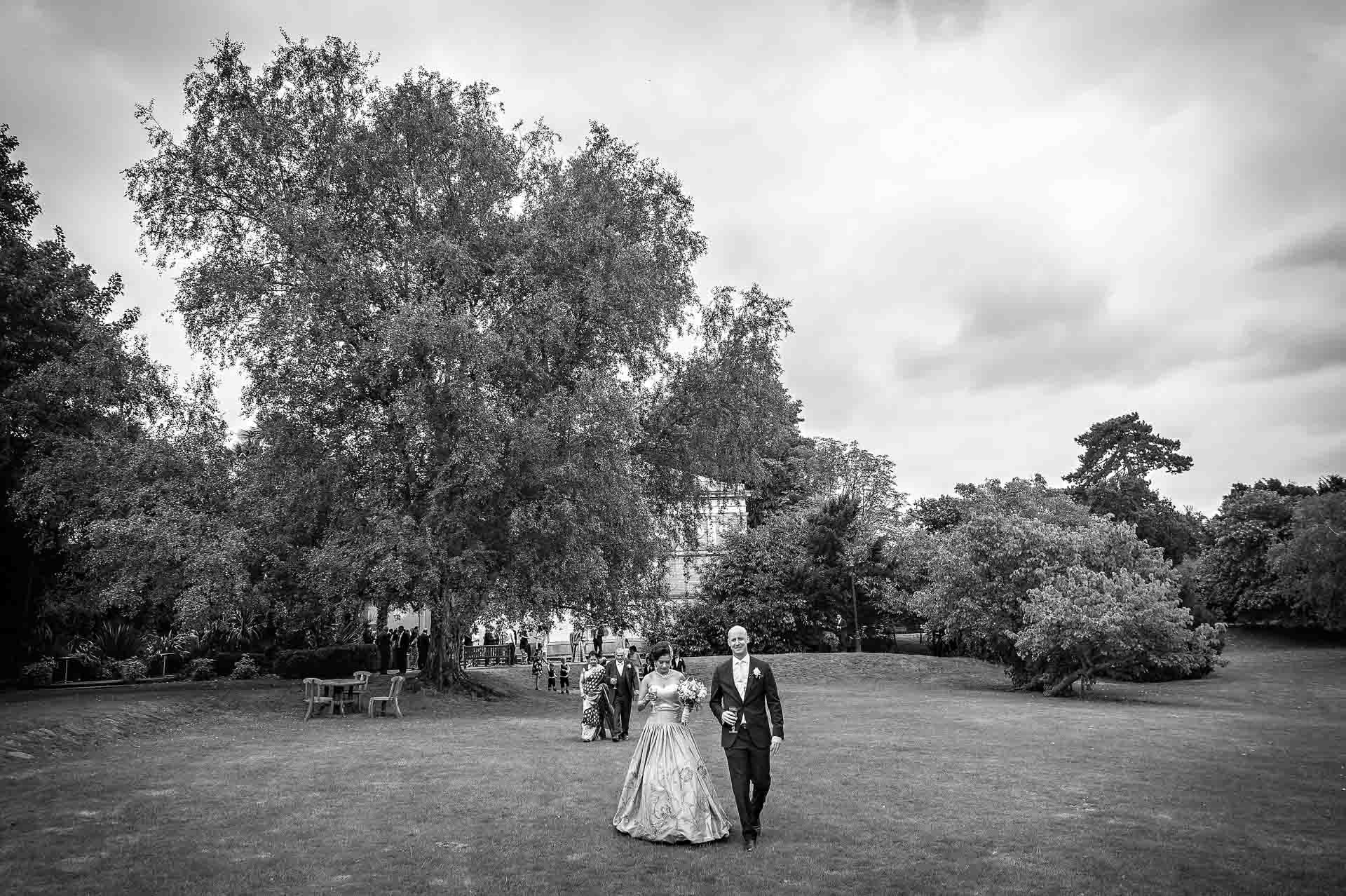 The couple walk across the lawn at Hampton Court House followed by their guests