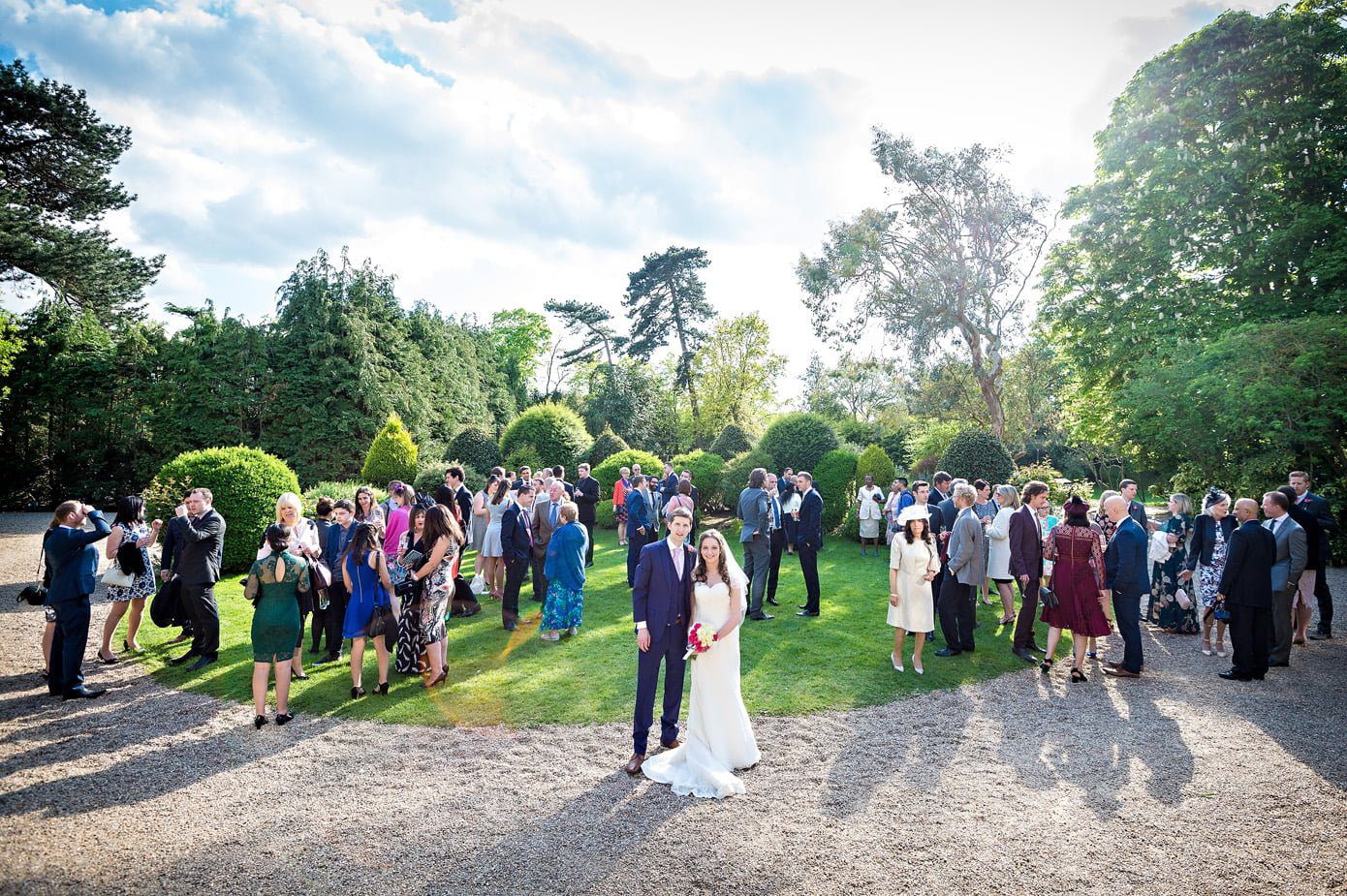 Couple portrait on lawn of Hampton Court House with wedding guests in background