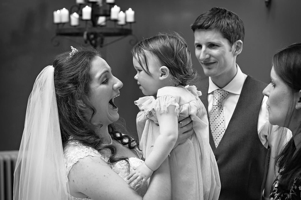 Bride lifting baby and pulling faces at wedding in Hampton Court House