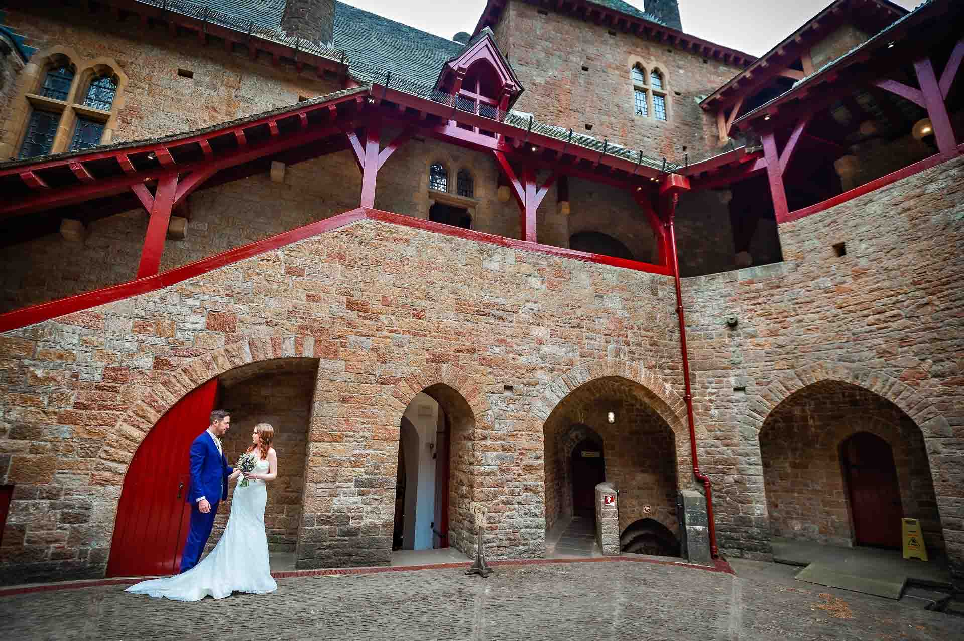 Newly married couple standing in courtyard of Castell Coch with arches in background - Guy Milnes Photography