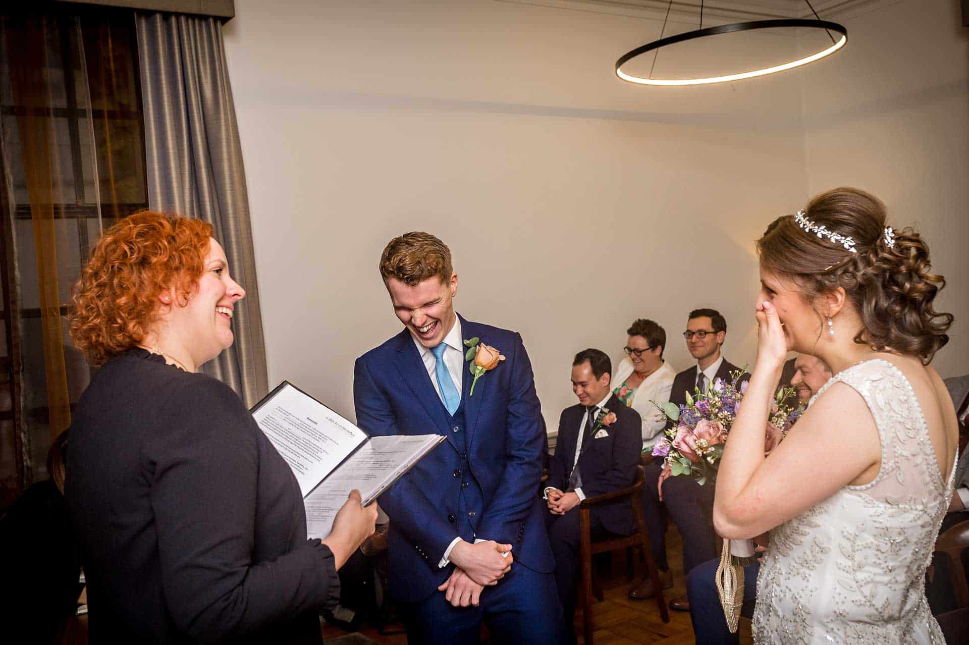 Bride at Groom laughing with registrar during Old Marylebone Town Hall wedding ceremony