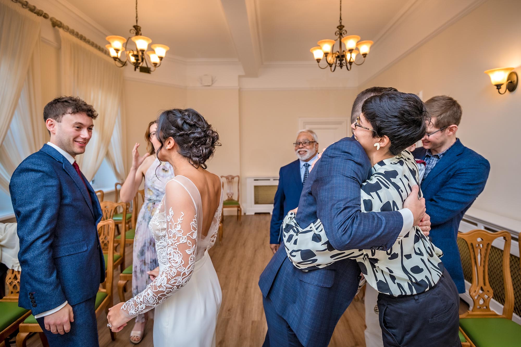 Grrom hugging family member whilst bride talks to another in Register Office Wedding