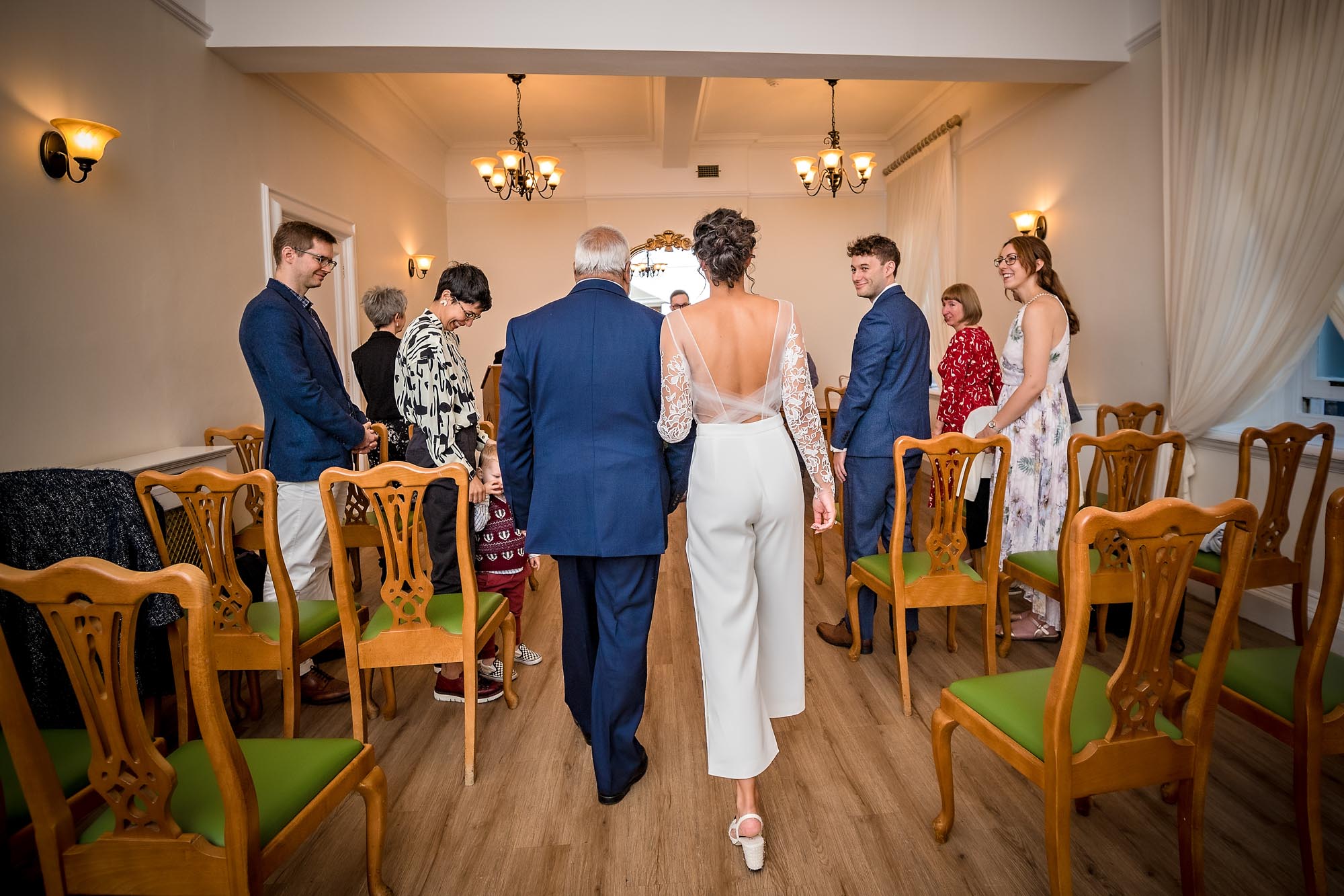 Shot from behind of father and bride daughter walking up the aisle in the Edwardian Room of Woolwich Town Hall