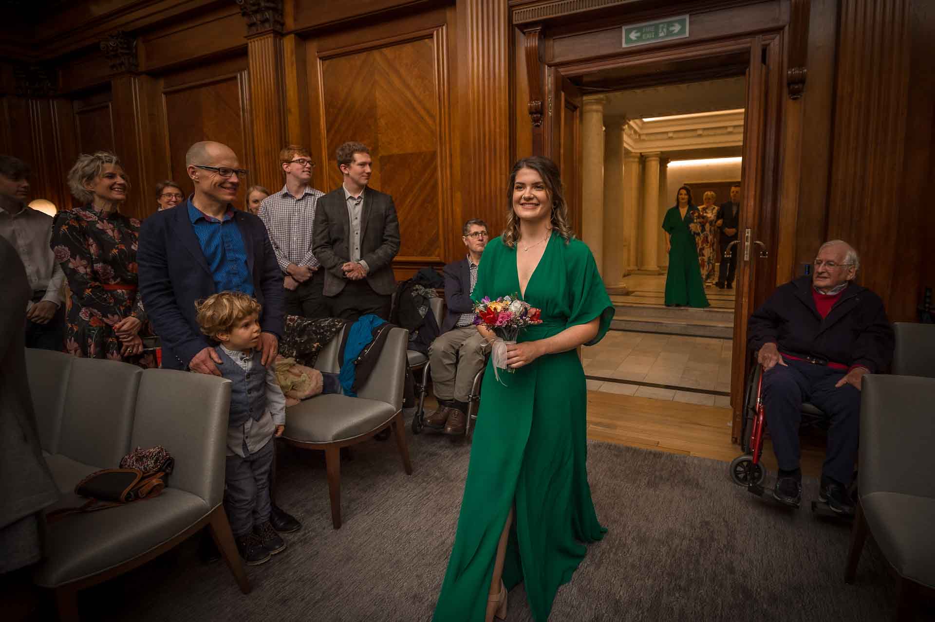 Smiling bride entering wedding ceremony whilst guests look on at Old Marylebone Town Hall