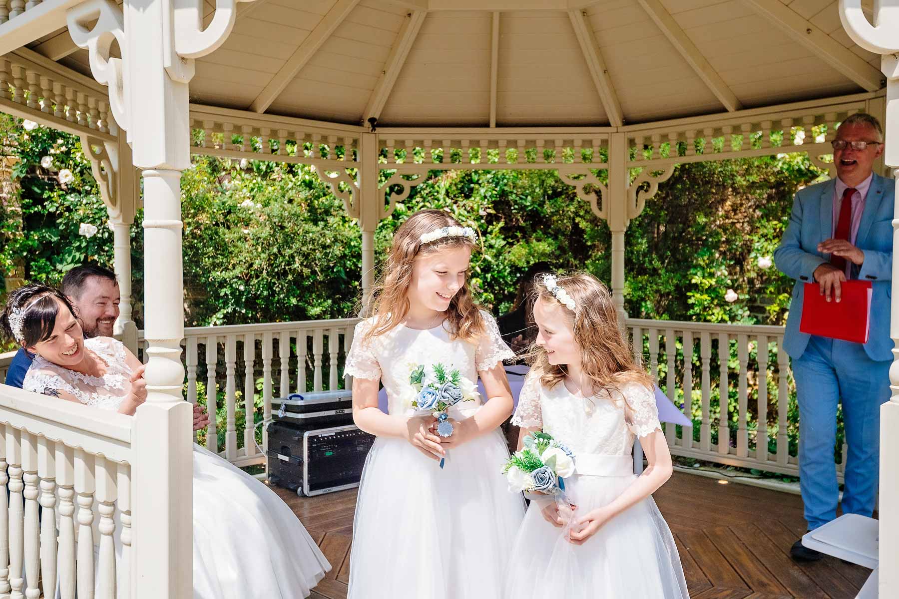 Two bridesmaids talking under Gazebo whilst couple watch at Morden Park House