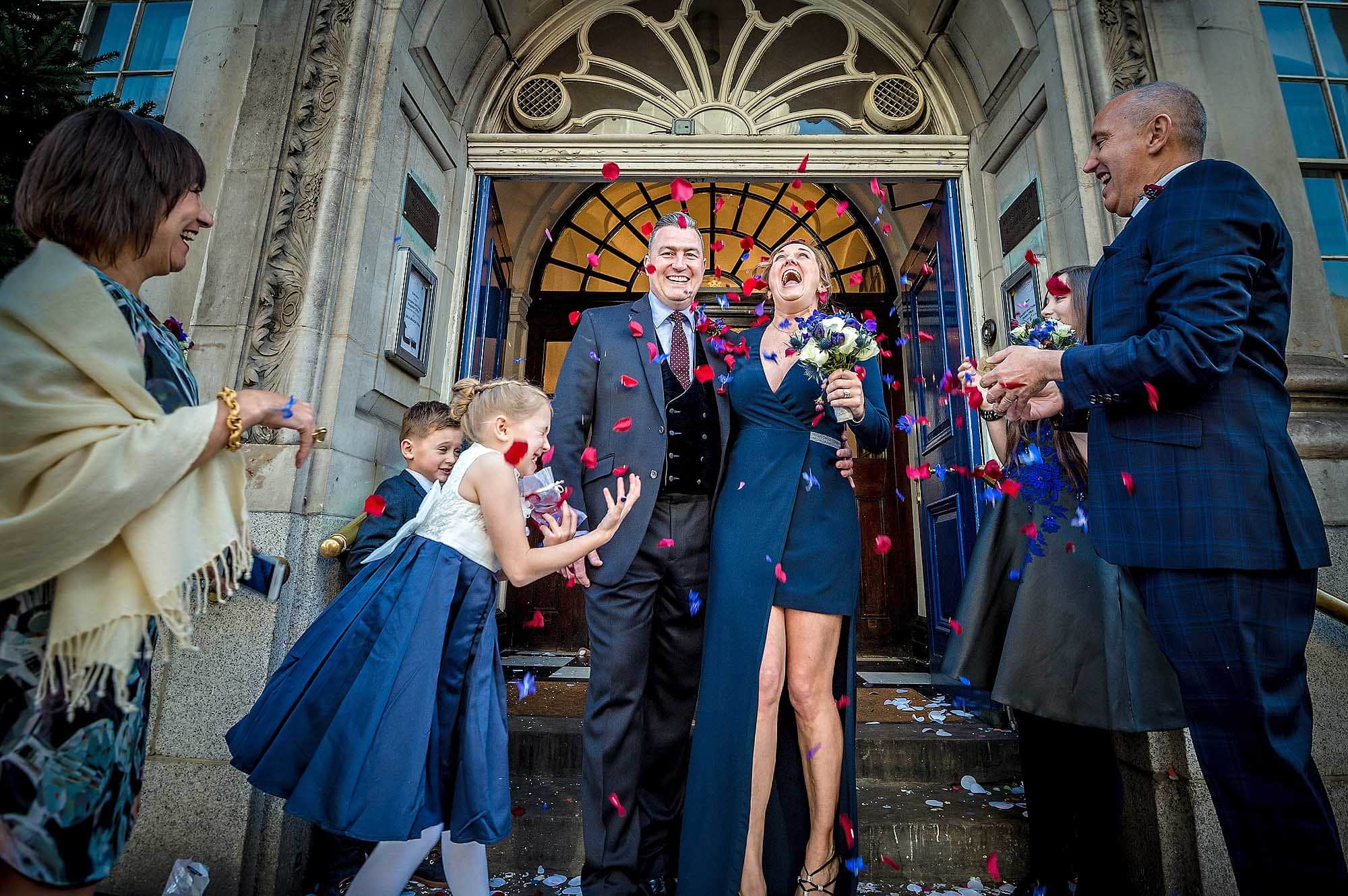 Bride laughing hysterically with groom as she exits Chelsea Old Town Hall in a shower of confetti