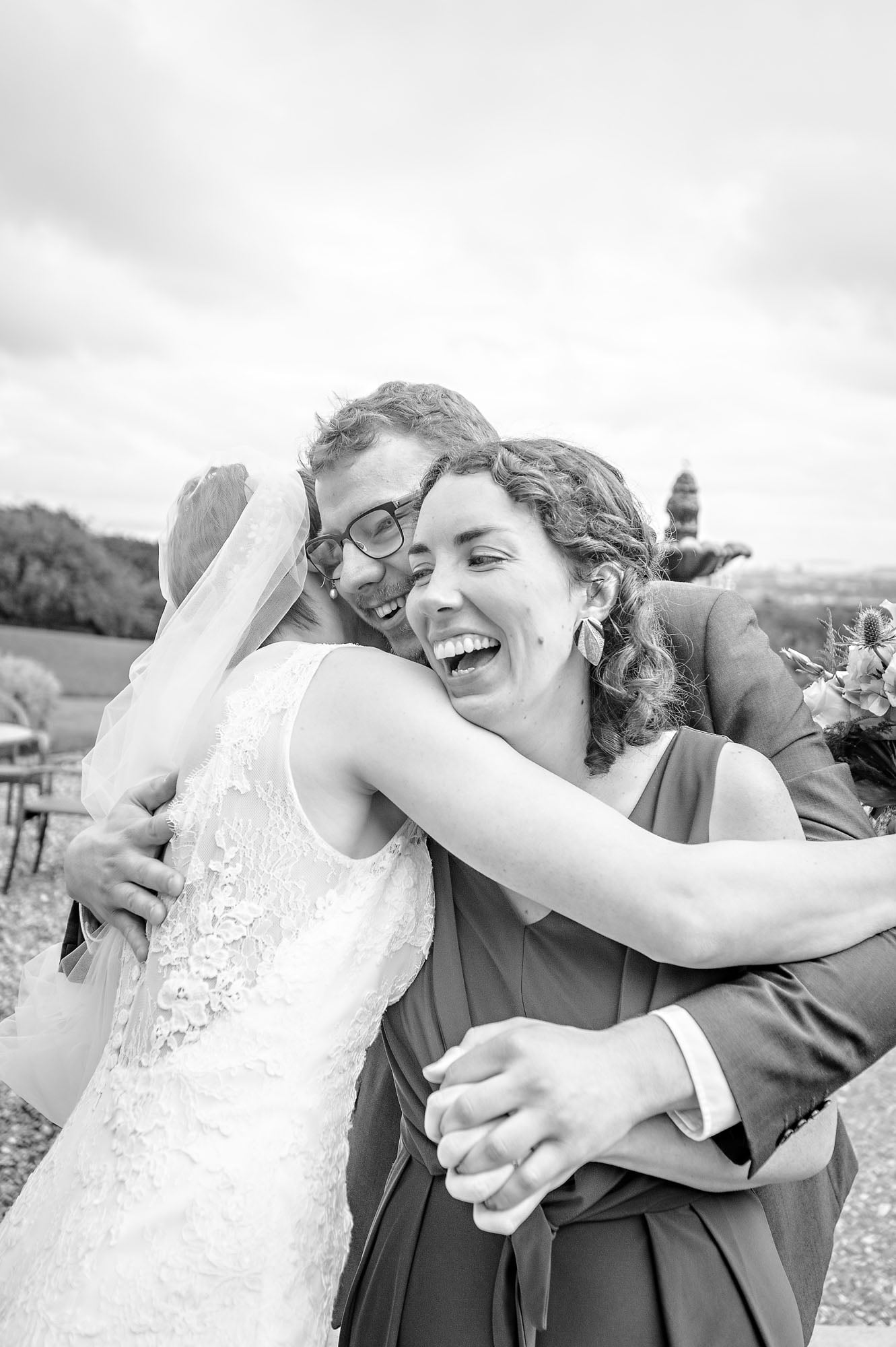 Bride hugs two smiling guests at wedding near Cardiff