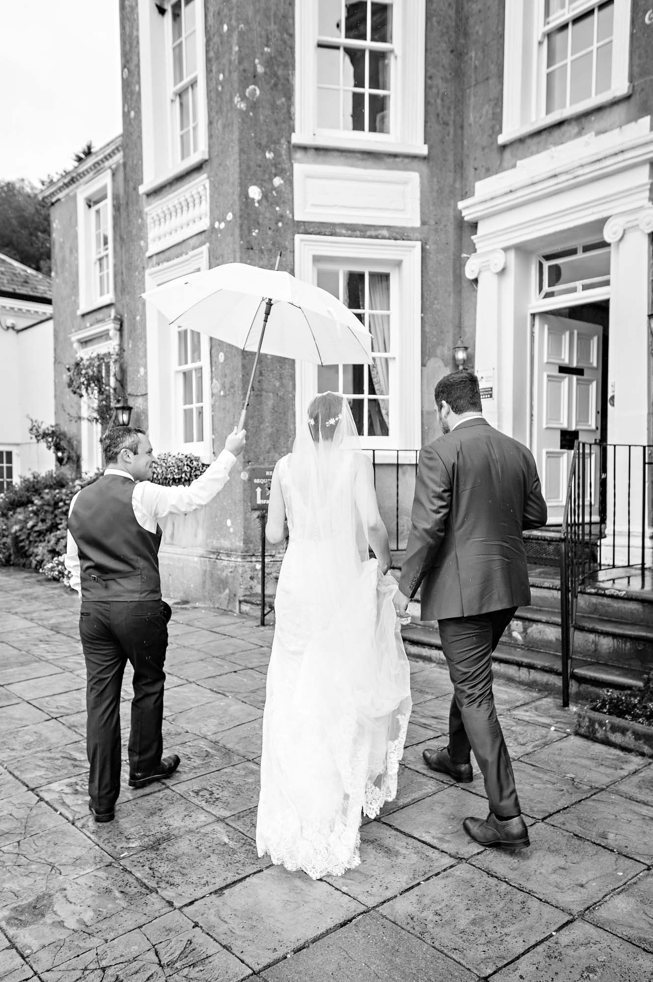 The newly-weds are shown into the New House Country Hotel under umbrella