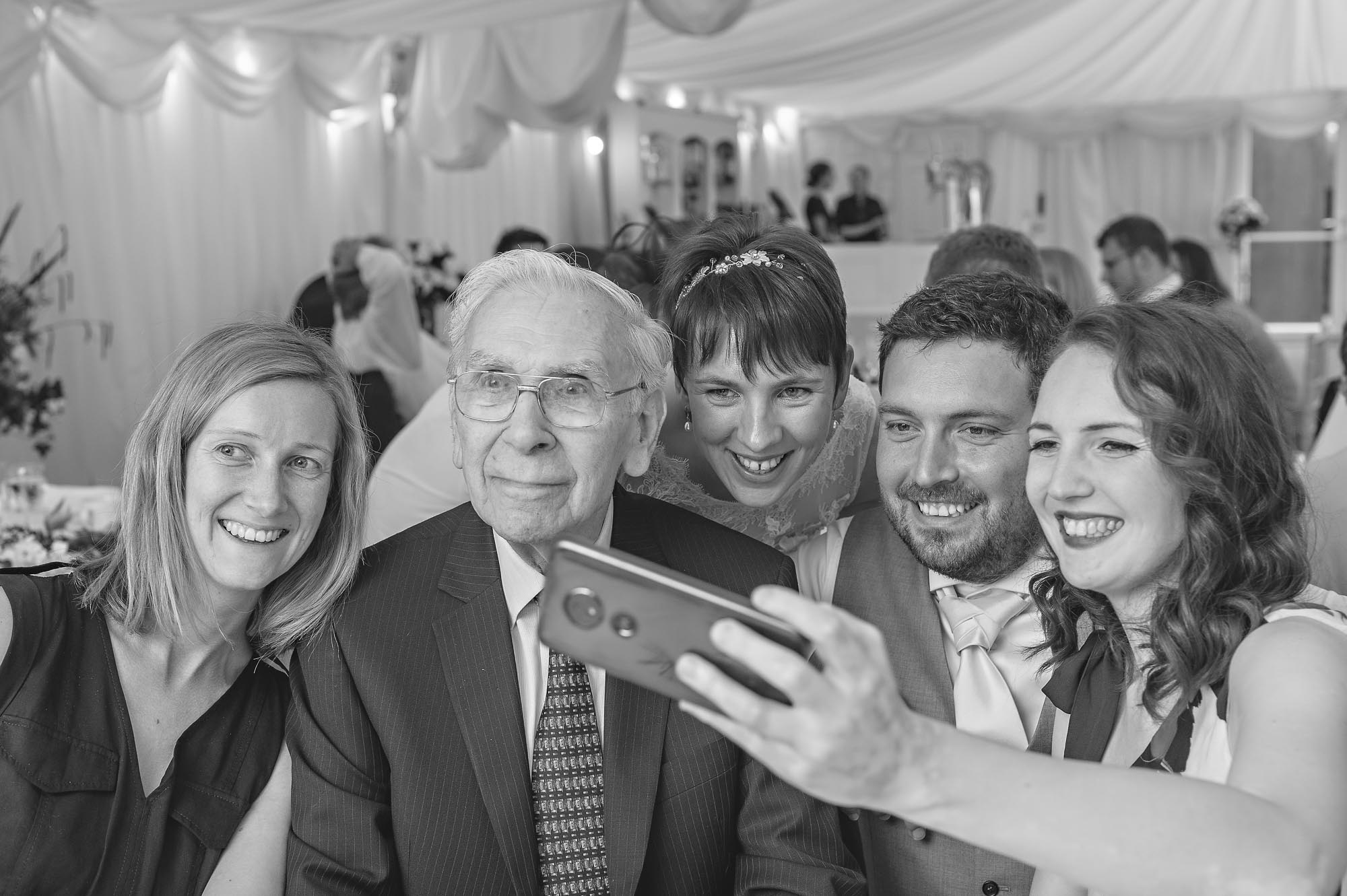 The bride, groom and three guests taking selfie at wedding