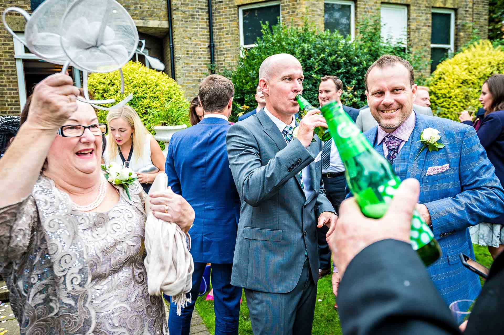 Woman at wedding raising fascinator whilstother guests drink