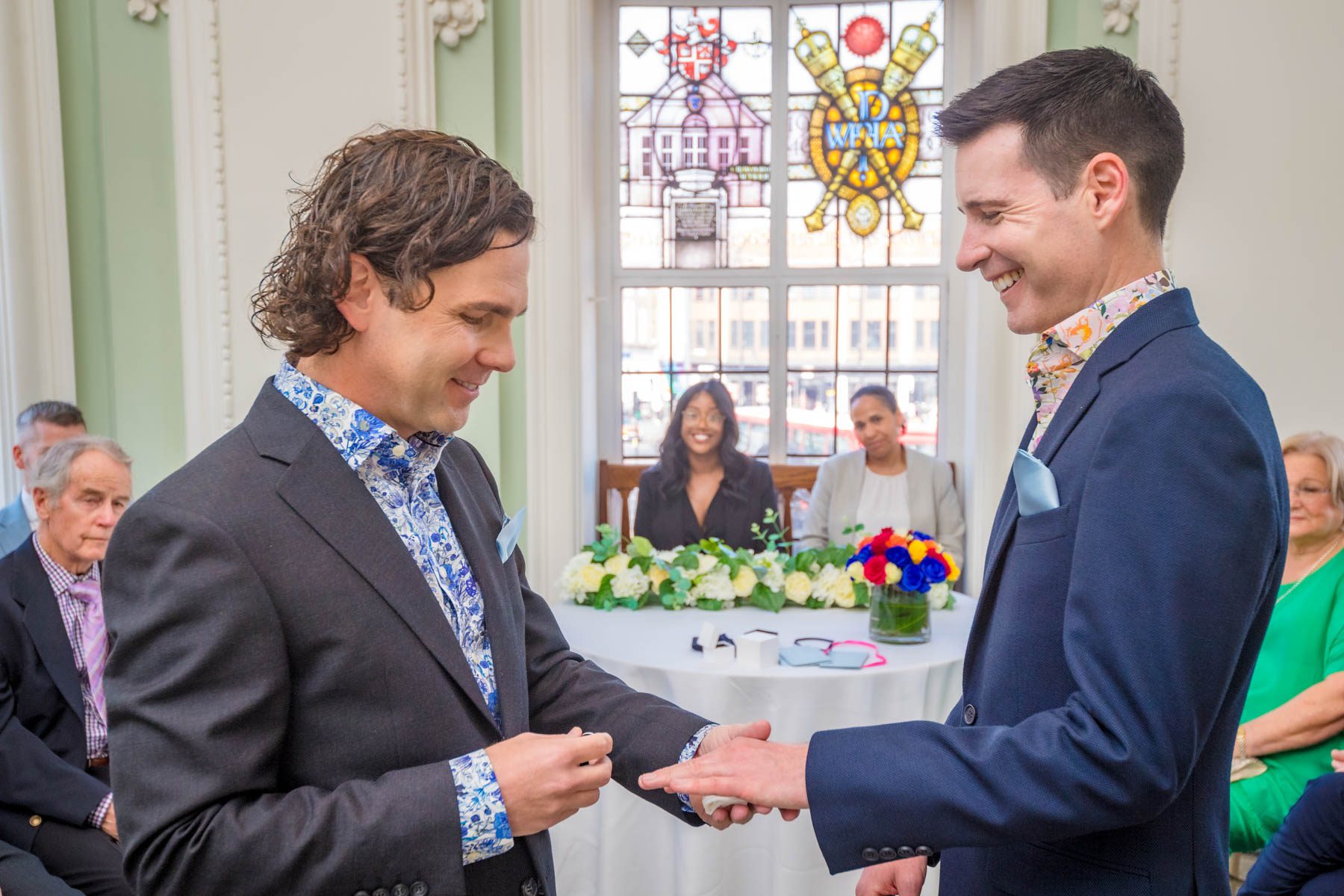 Groom's smiling at a Lambeth Town Hall LGBTQ+ wedding as one places a ring on the others finger.
