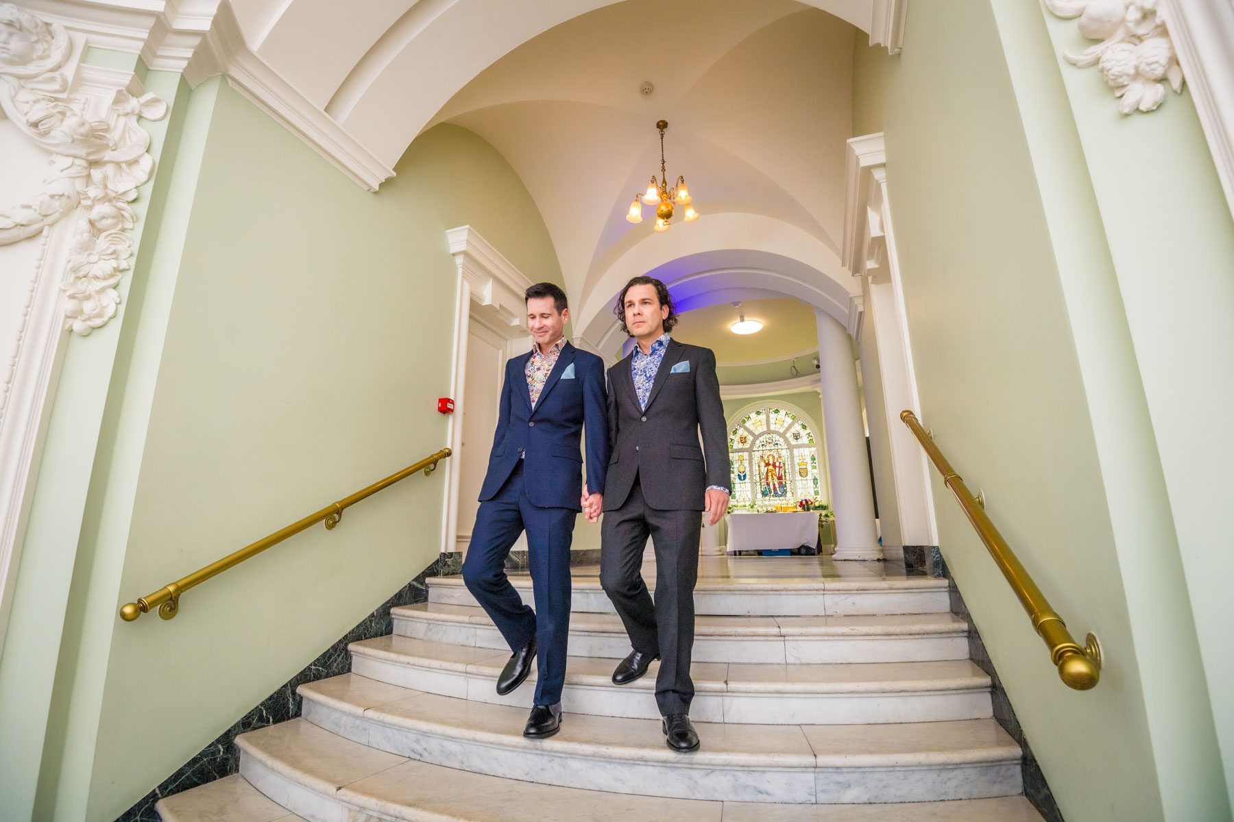 The grooms descend the staircase to their wedding ceremony in the Circular Hall at Lambeth Town Hall.