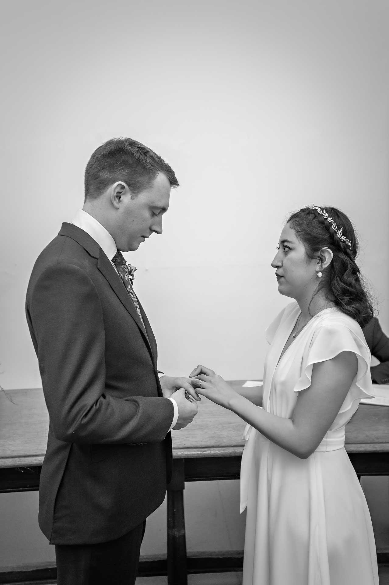 Bride watches groom intently as she places the ring on his finger