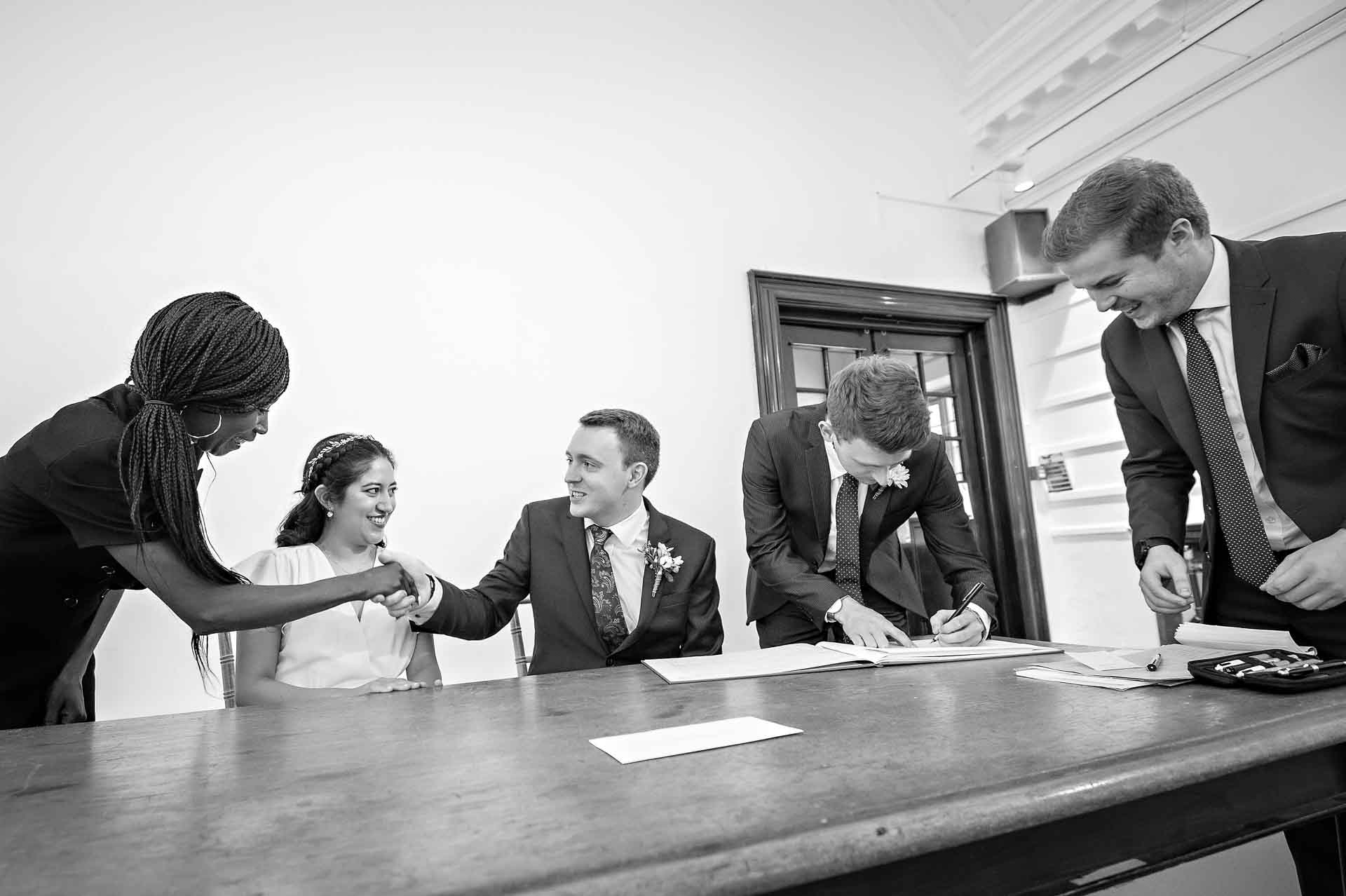 A witness signs the register as the registrar shakes hands with the groom at Fulham Library wedding