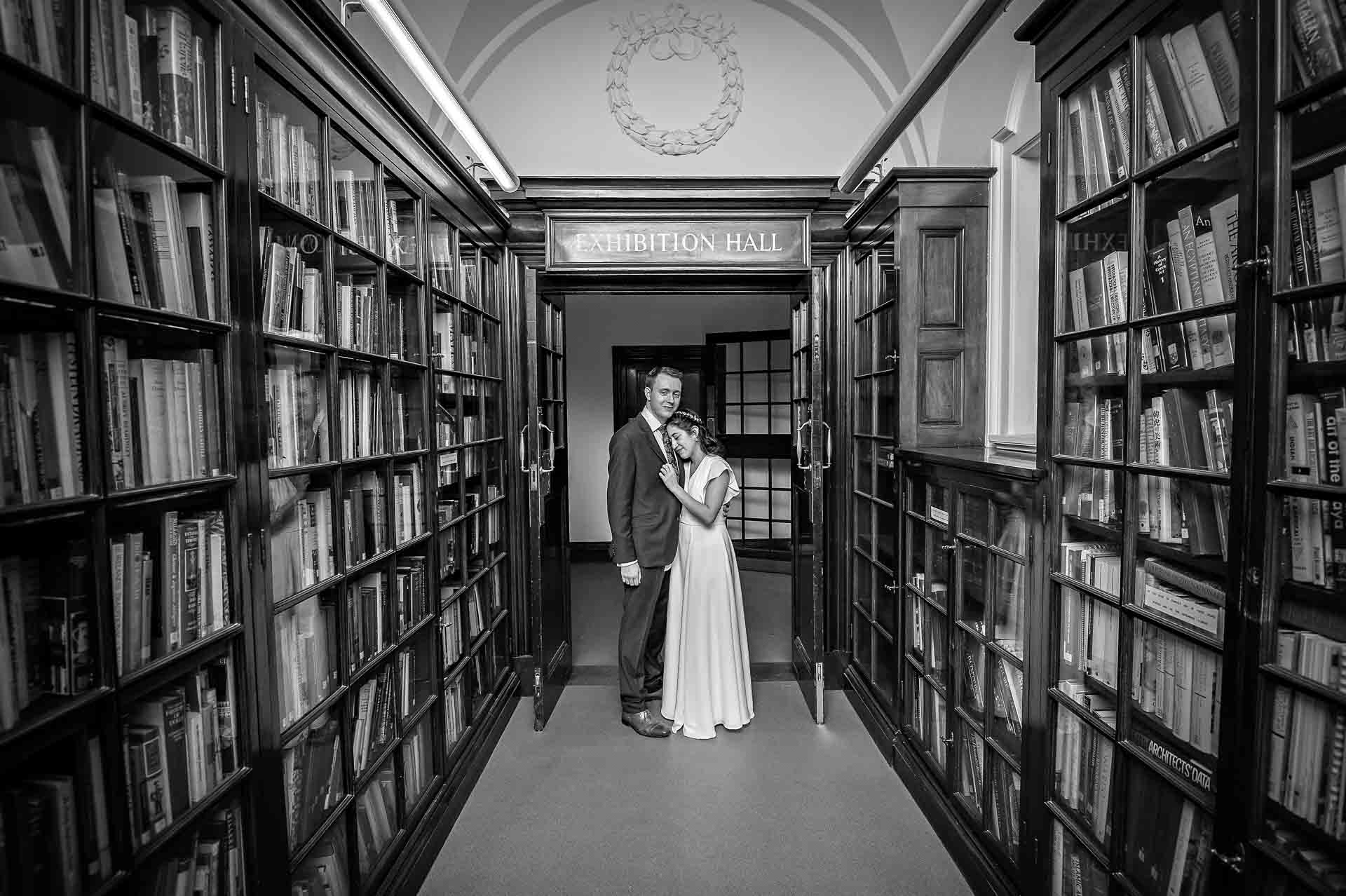 Bride rests head on groom's chest at end of the Fine Art Collection Corridor in Fulham Library