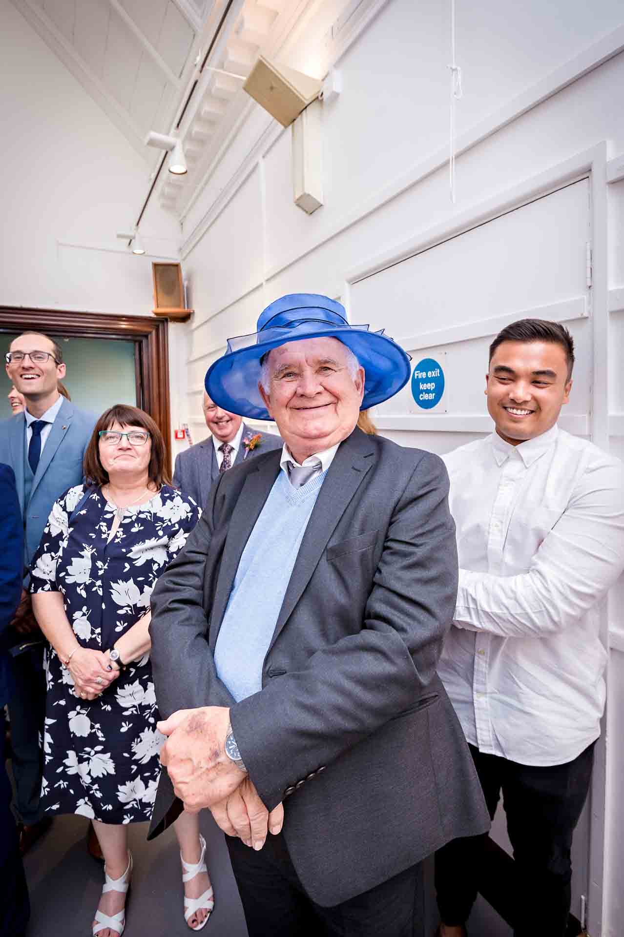 Older man at wedding wearing blue lady's hat at wedding