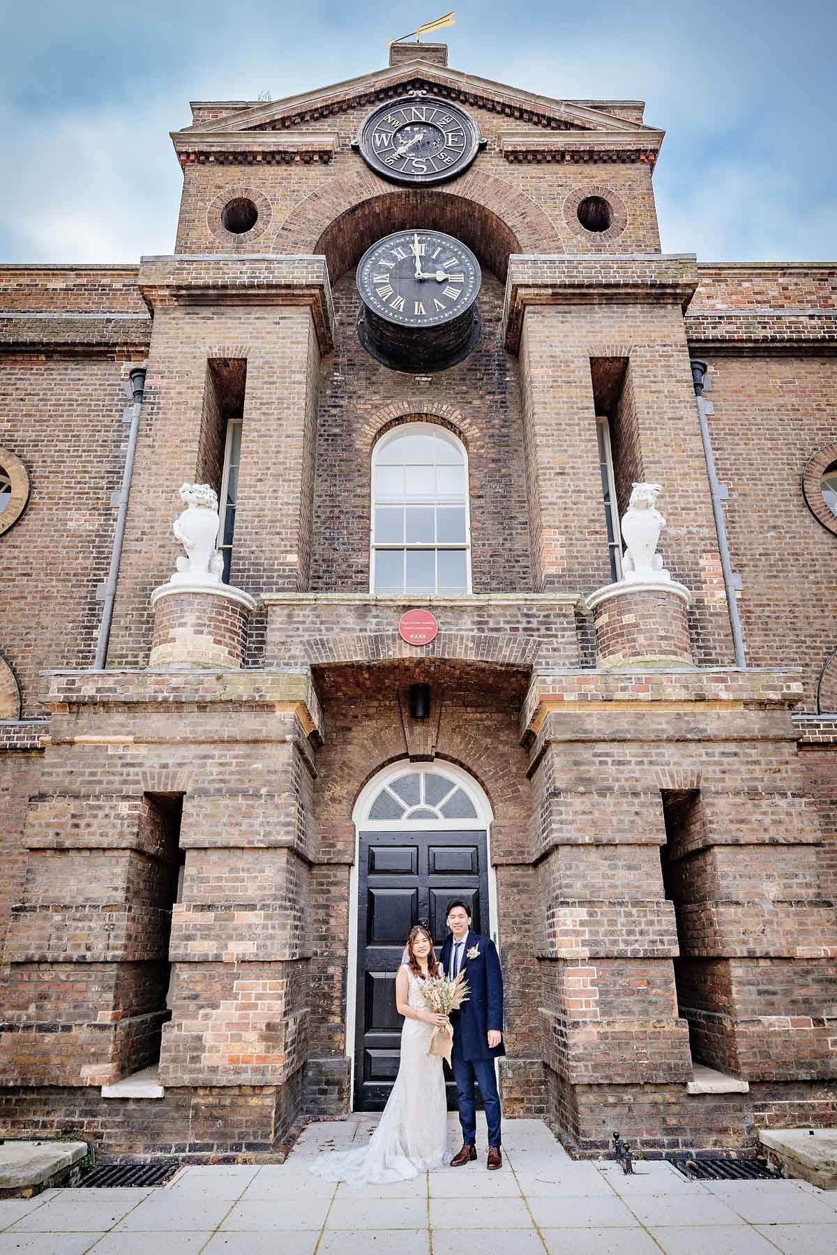 Newly-weds pose in front of building with clock and weathervane, Woolwich
