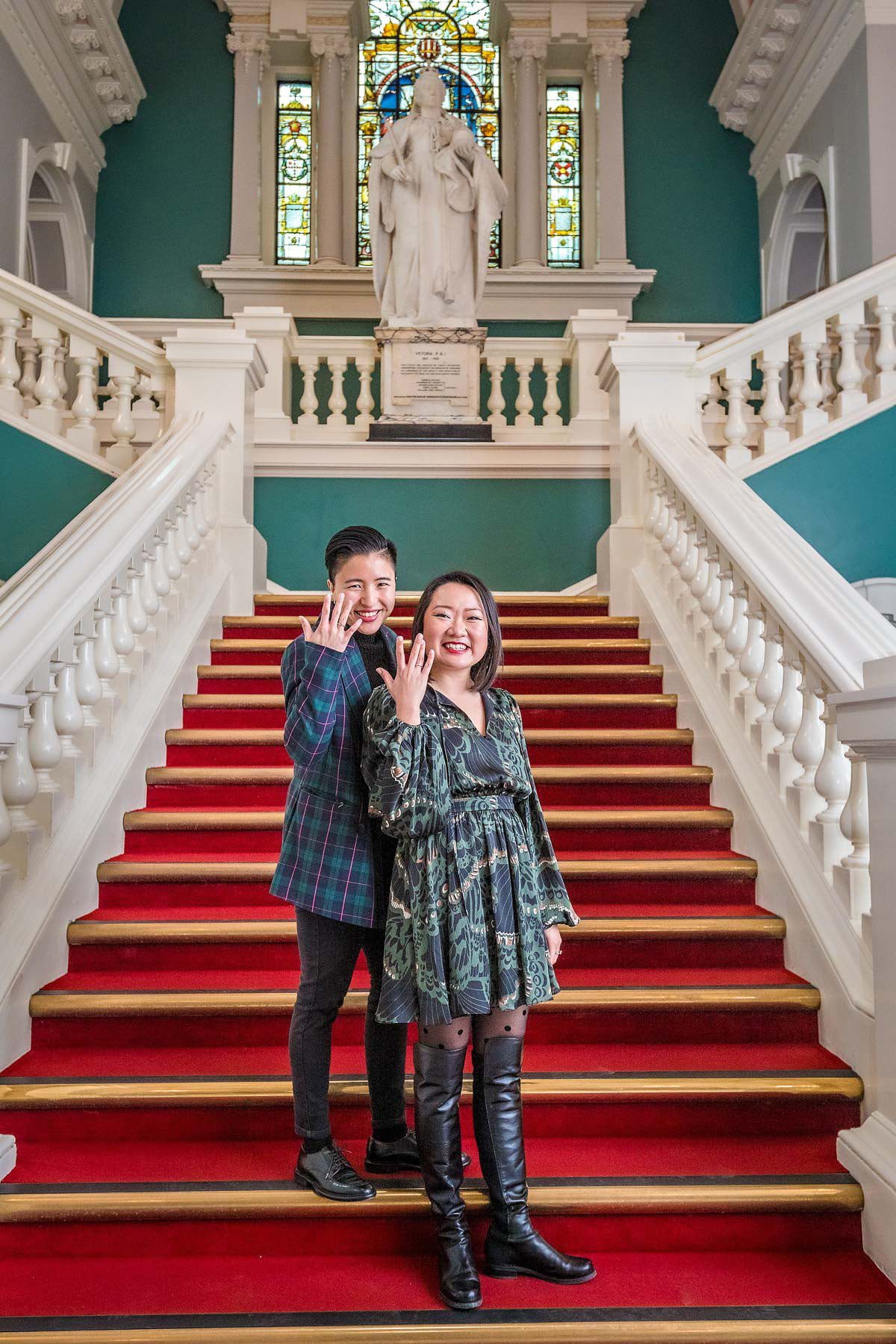 A female couple pose on the stairs of the Victoria Hall in Woolwich to show off their wedding rings.