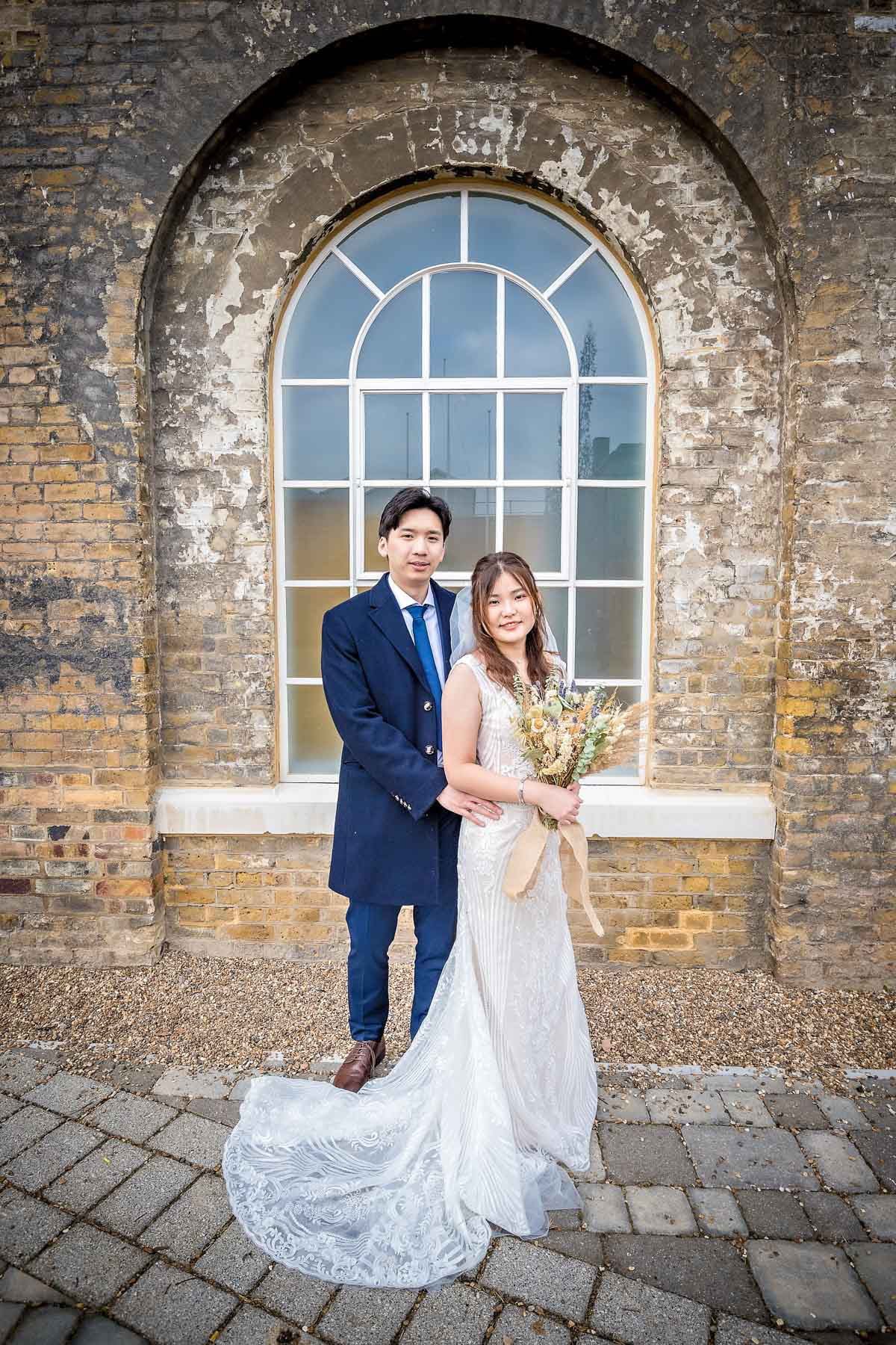 A wedding couple pose outside an arched window with flaky paintwork in Woolwich