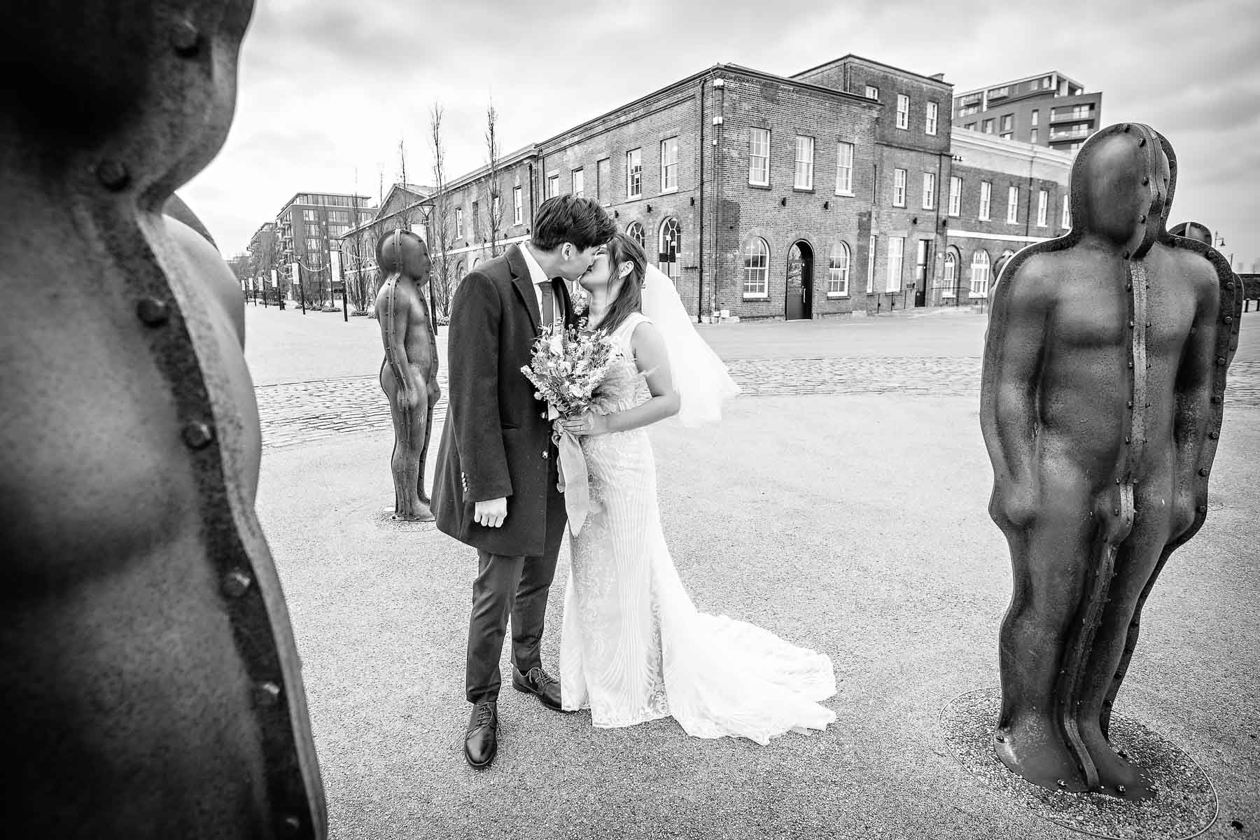 A newlywed couple kiss in between two statues at Woolwich's Royal Arsenal Heritage Site