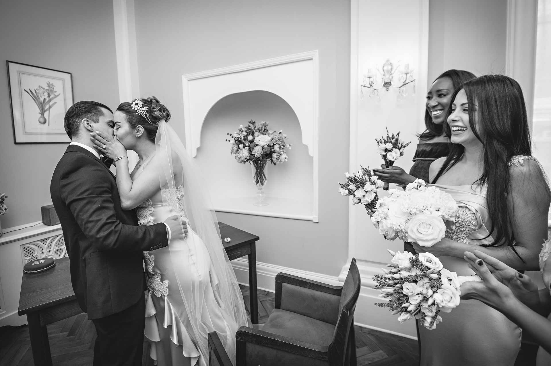 Bride and Groom kiss as guests look on at wedding in Rossetti Room, Chelsea