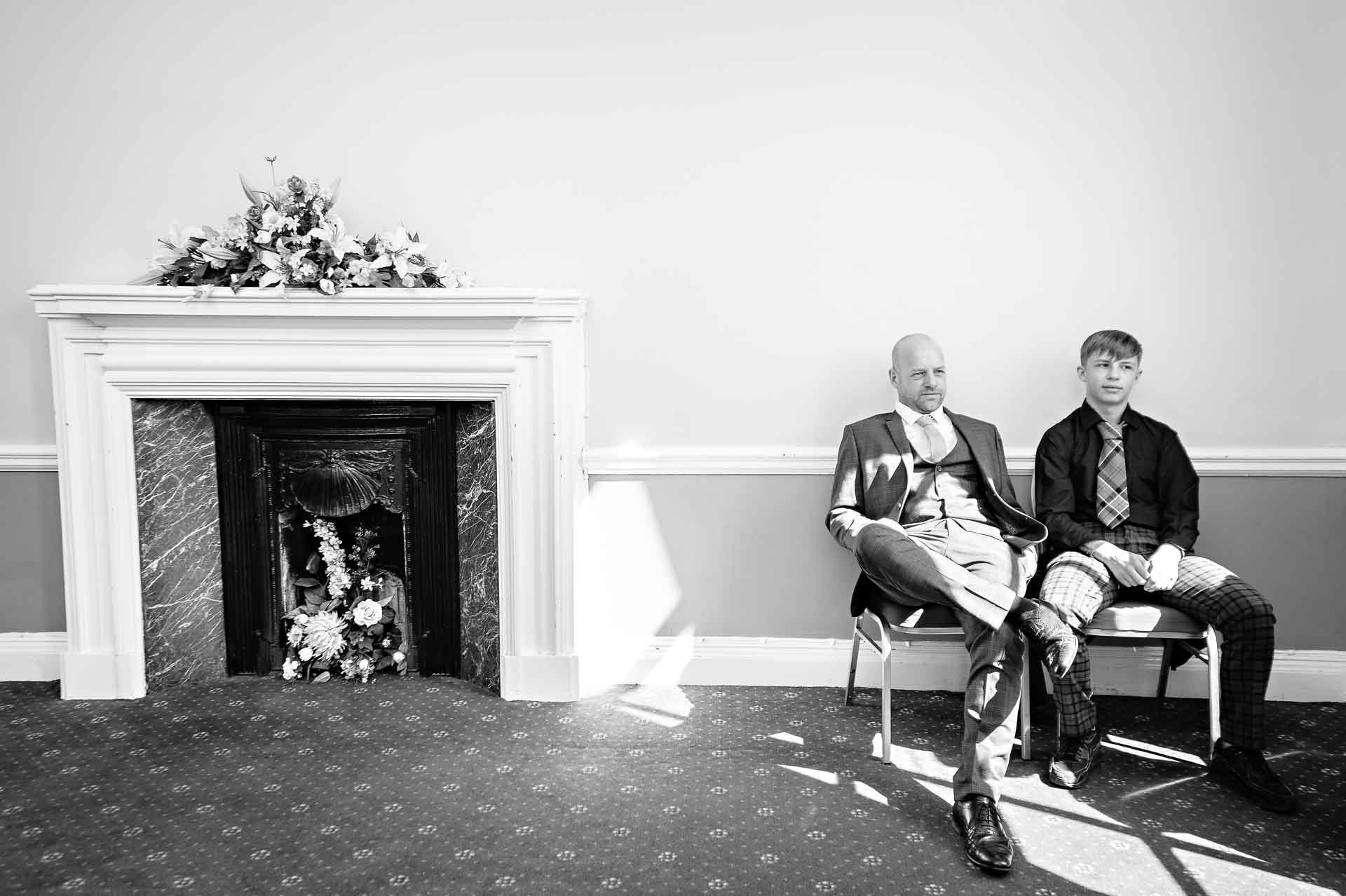 Two men sitting in waiting room of Cardiff City Hall next to ornate fireplace