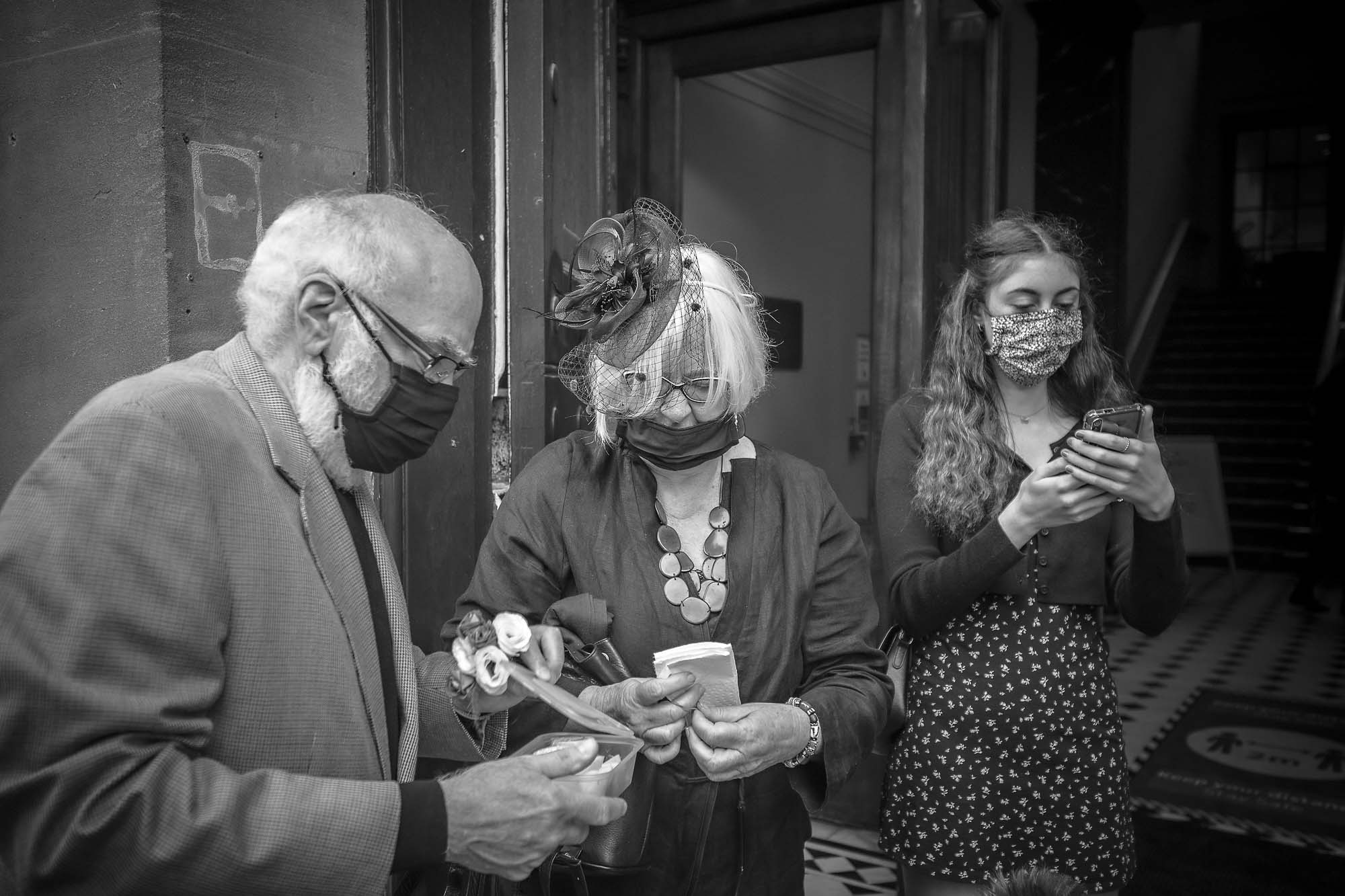 Three family memebers with COVID-19 masks on phones outside Bristol Old Council House