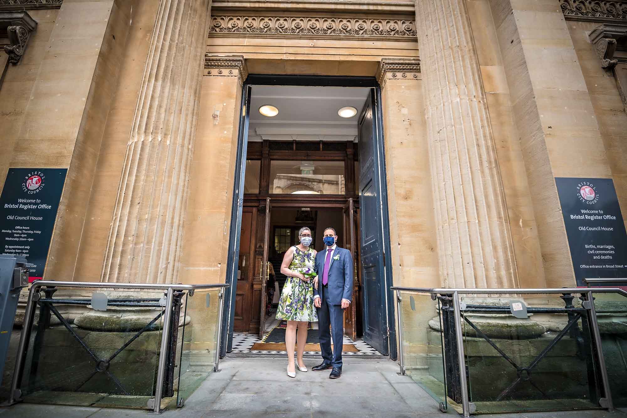 Newly-wedded couple with face masks posing outside Bristol Old Council House