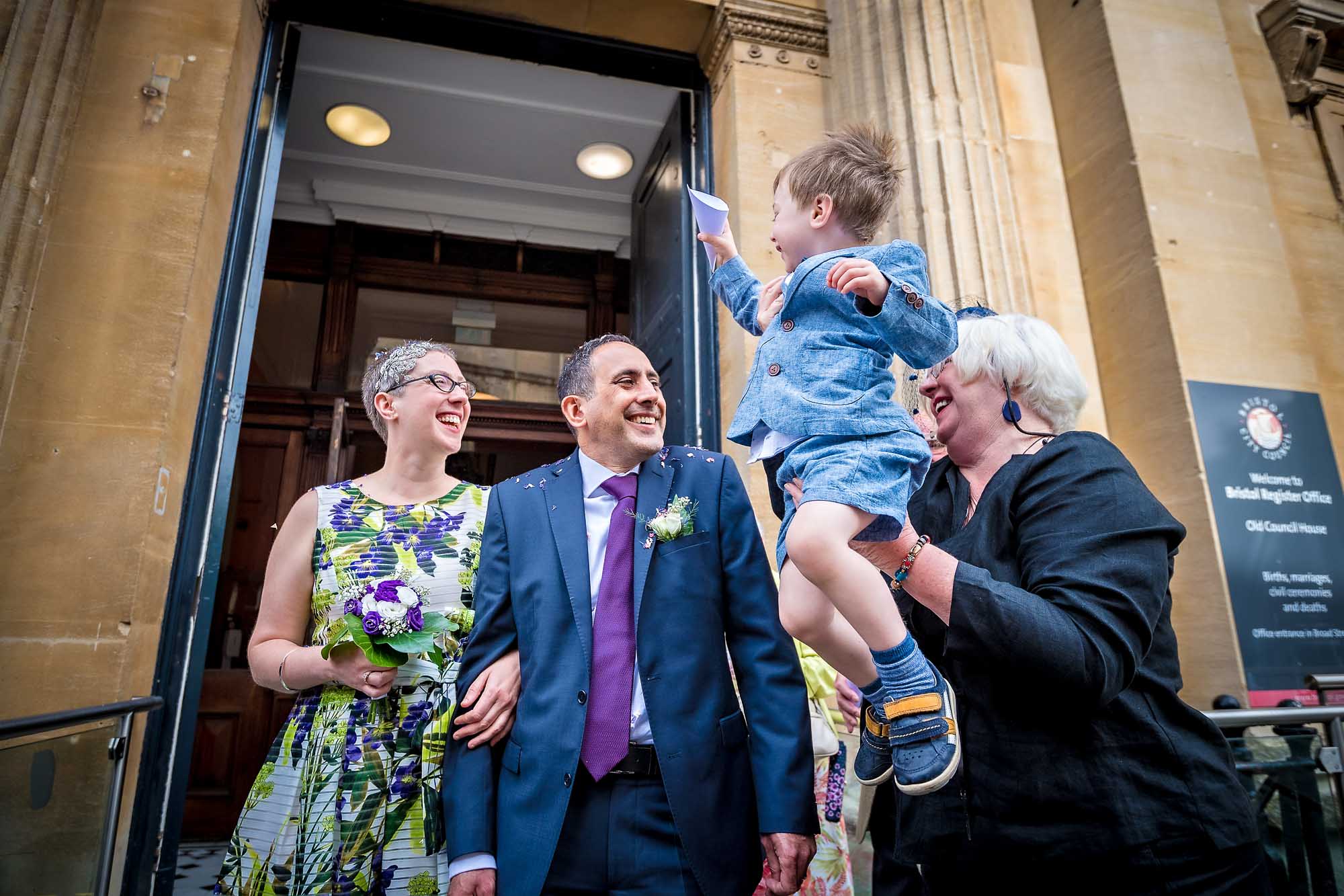 Little boy being held about to pour confetti on newly-weds in Bristol
