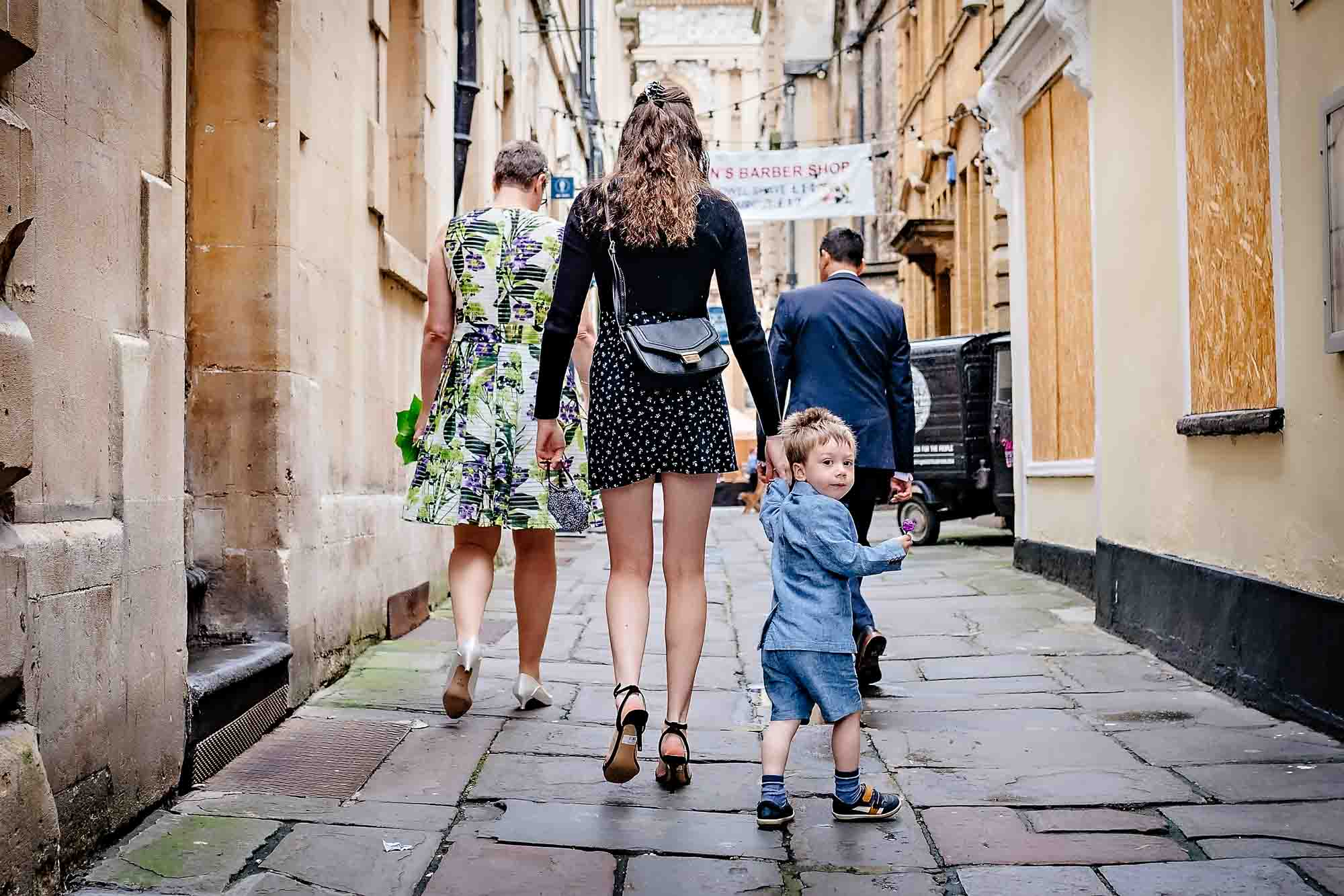Little boy looking back at camera whilst family walk way at Bristol wedding