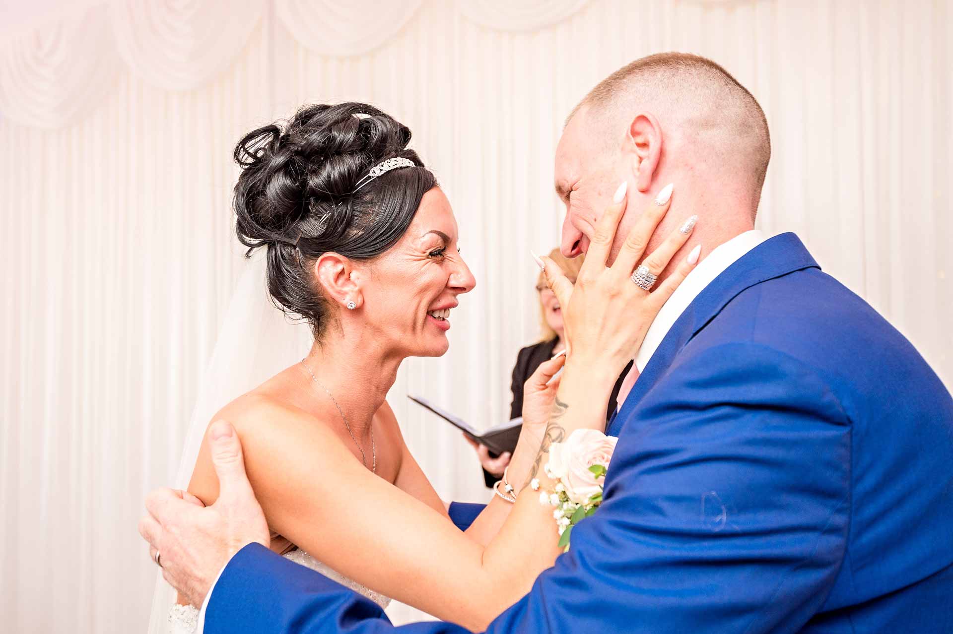 Bride laughing and holding groom's face at the end of the wedding ceremony