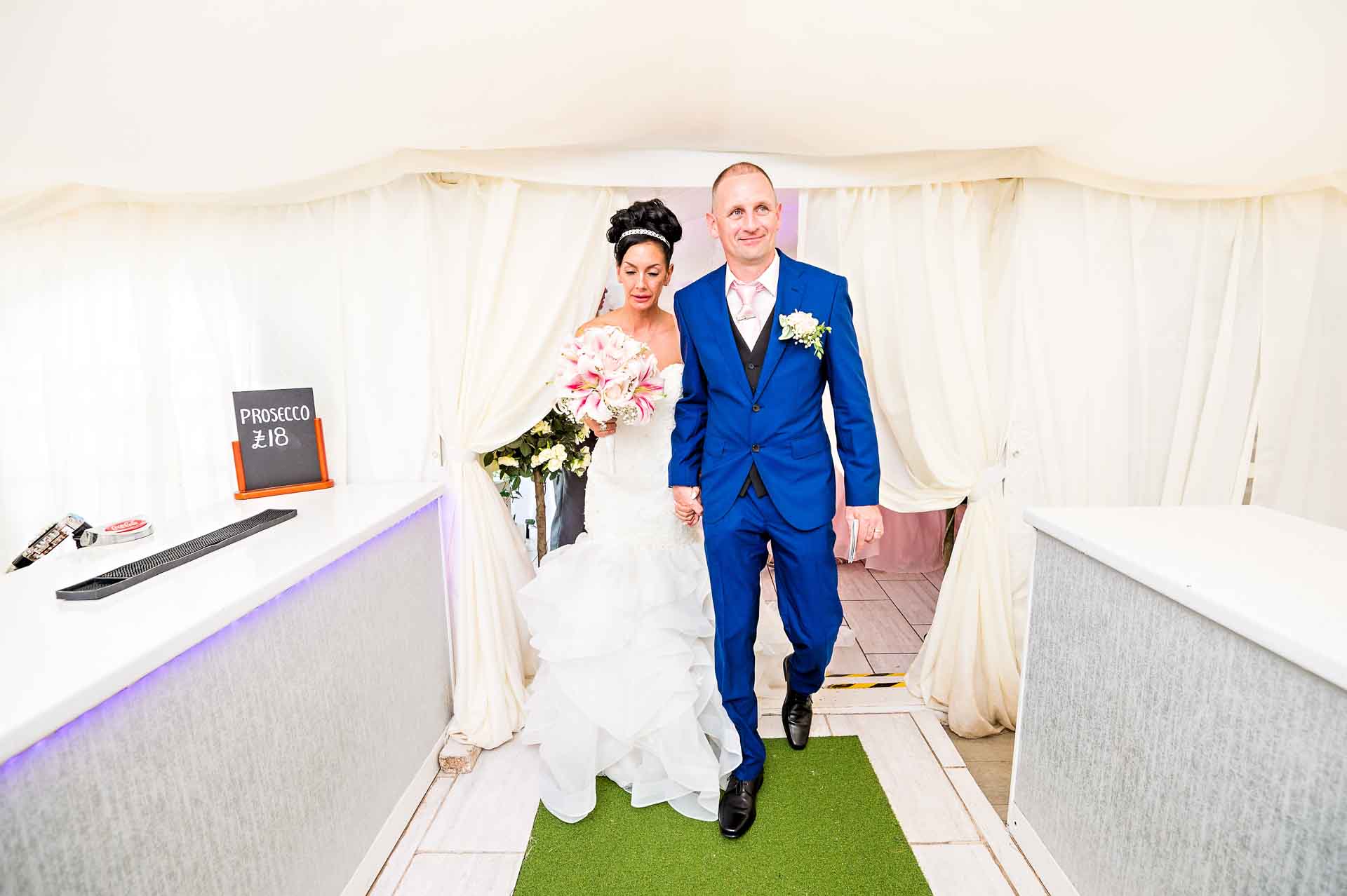 The bride and groom leave their wedding ceremony in Marquee at Ridgeway Golf Club through the bar