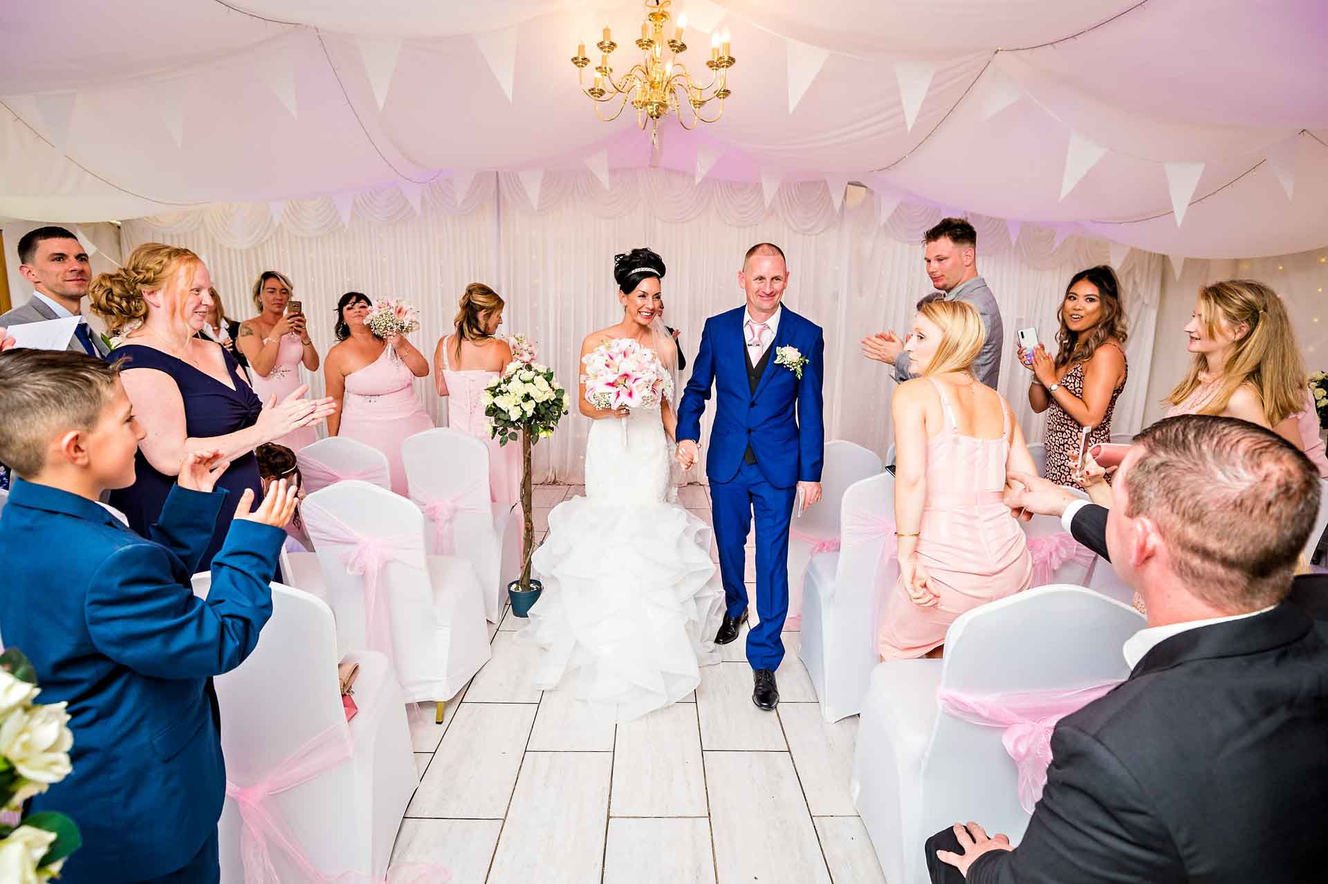 The bride and groom walk back up the aisle in the Marquee at Ridgeway Golf Club