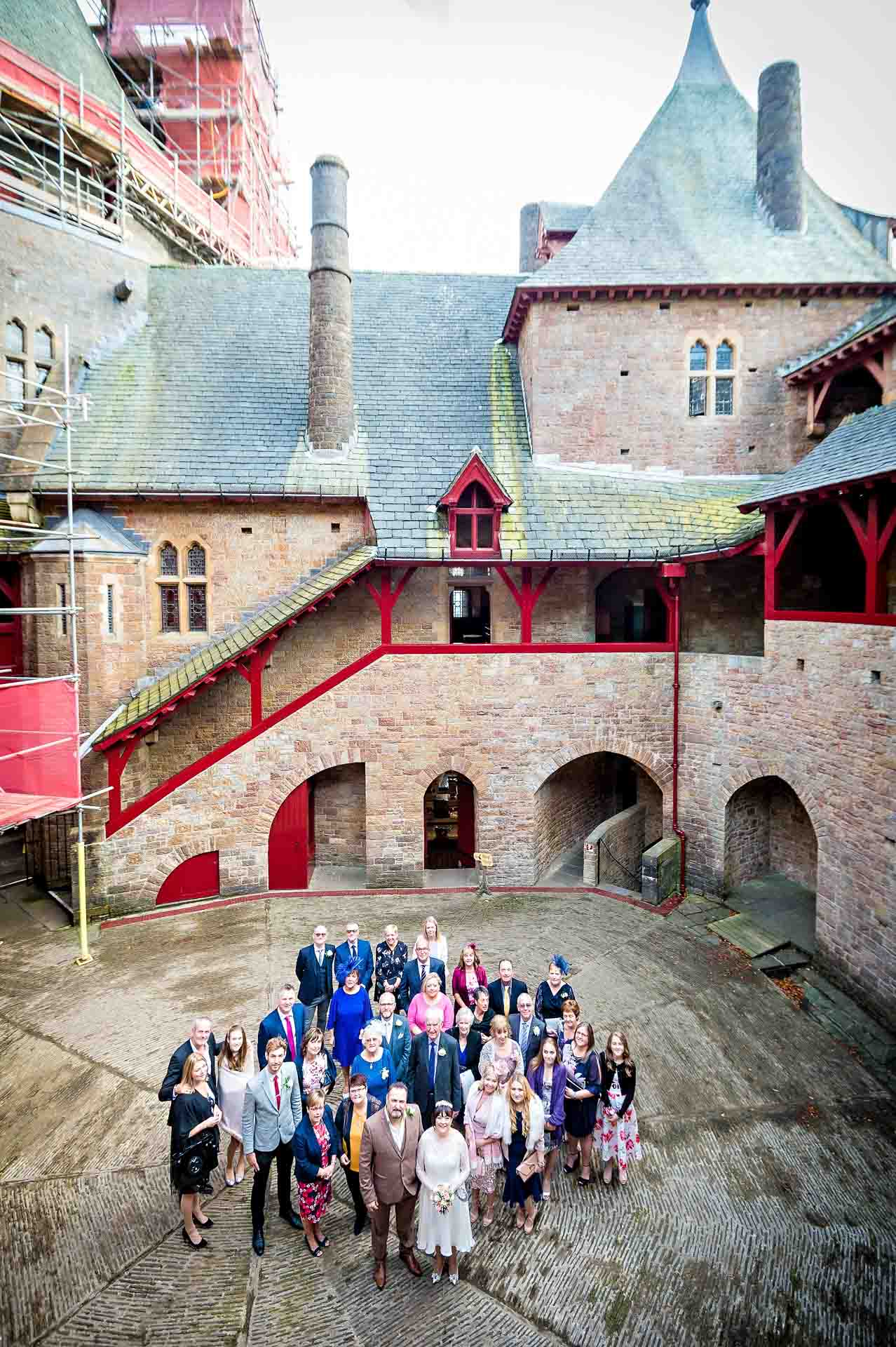 Group portrait taken of whole wedding party from above showing the architecture at Castell Coch in the background
