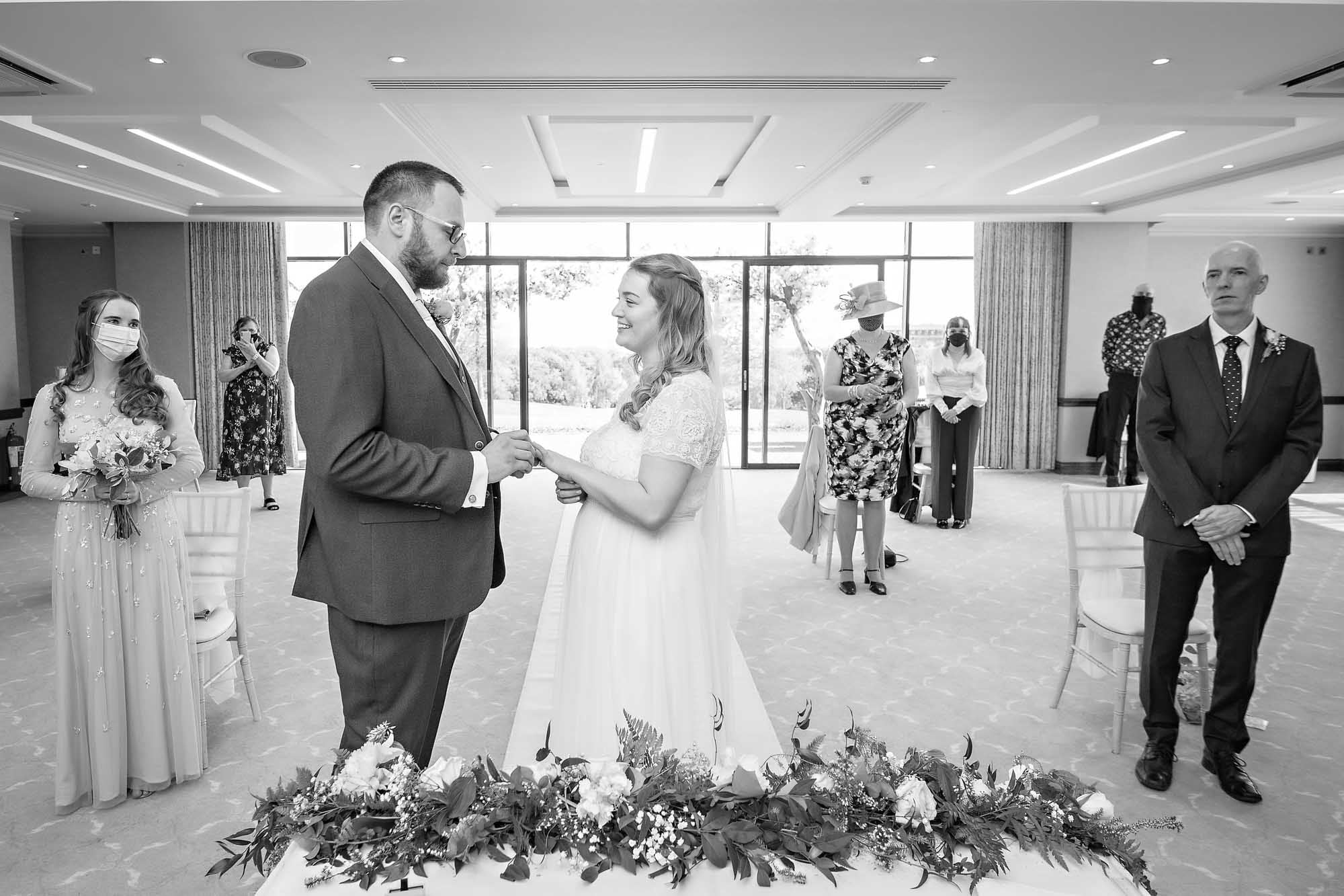 The groom places the ring on the finger of his bride as guests look on in Celtic Manor Resort's Via Julia Suite