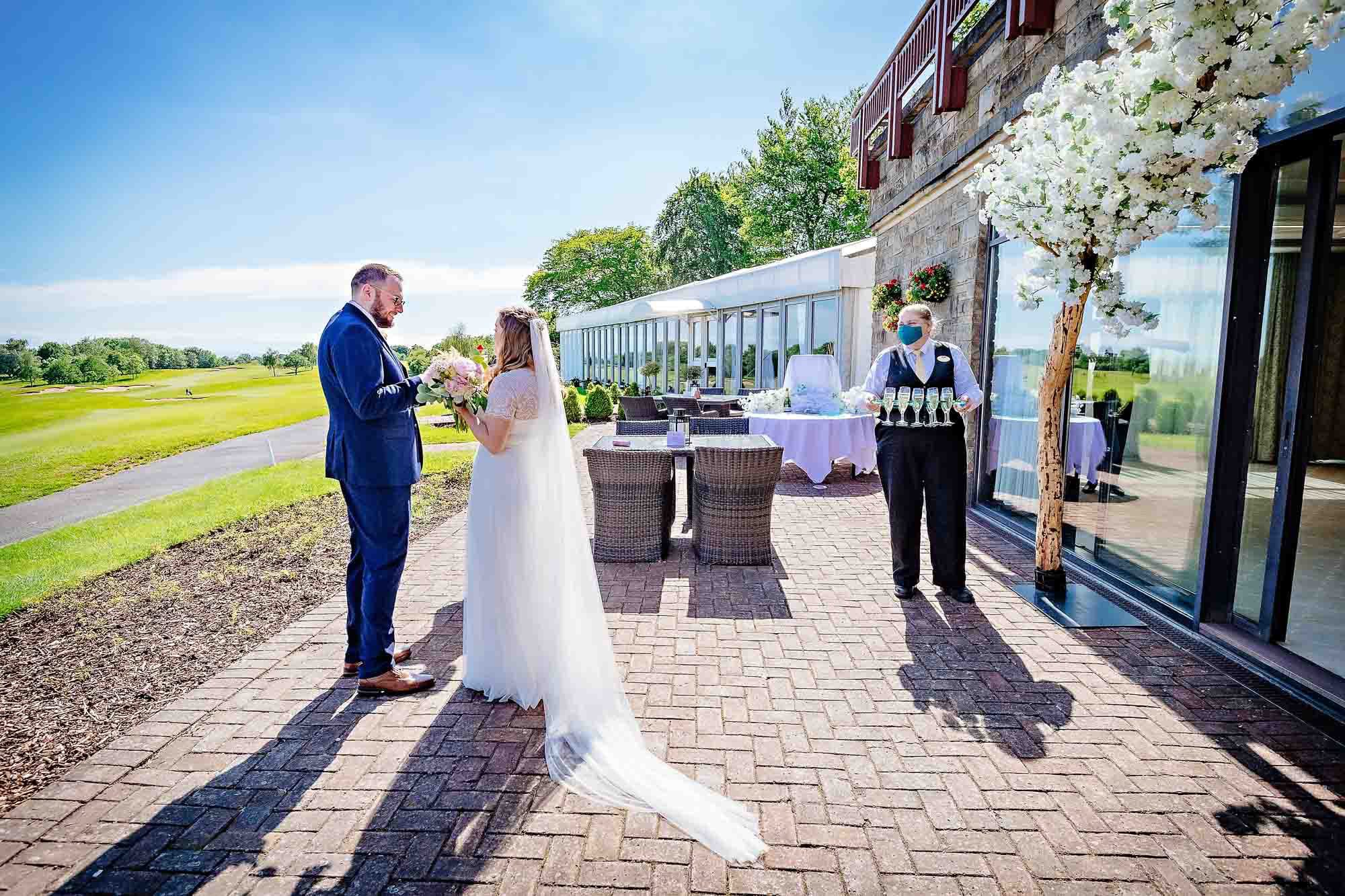 The newlyweds stand together near a waitress about to serve Champagne outside the Via Julia Suite, Celtic Manor Resort