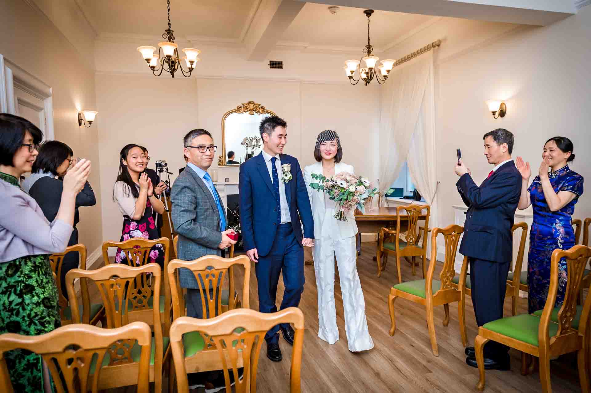 The happy couple leaving the Edwardian Room in Woolwich Town Hall with guests clapping