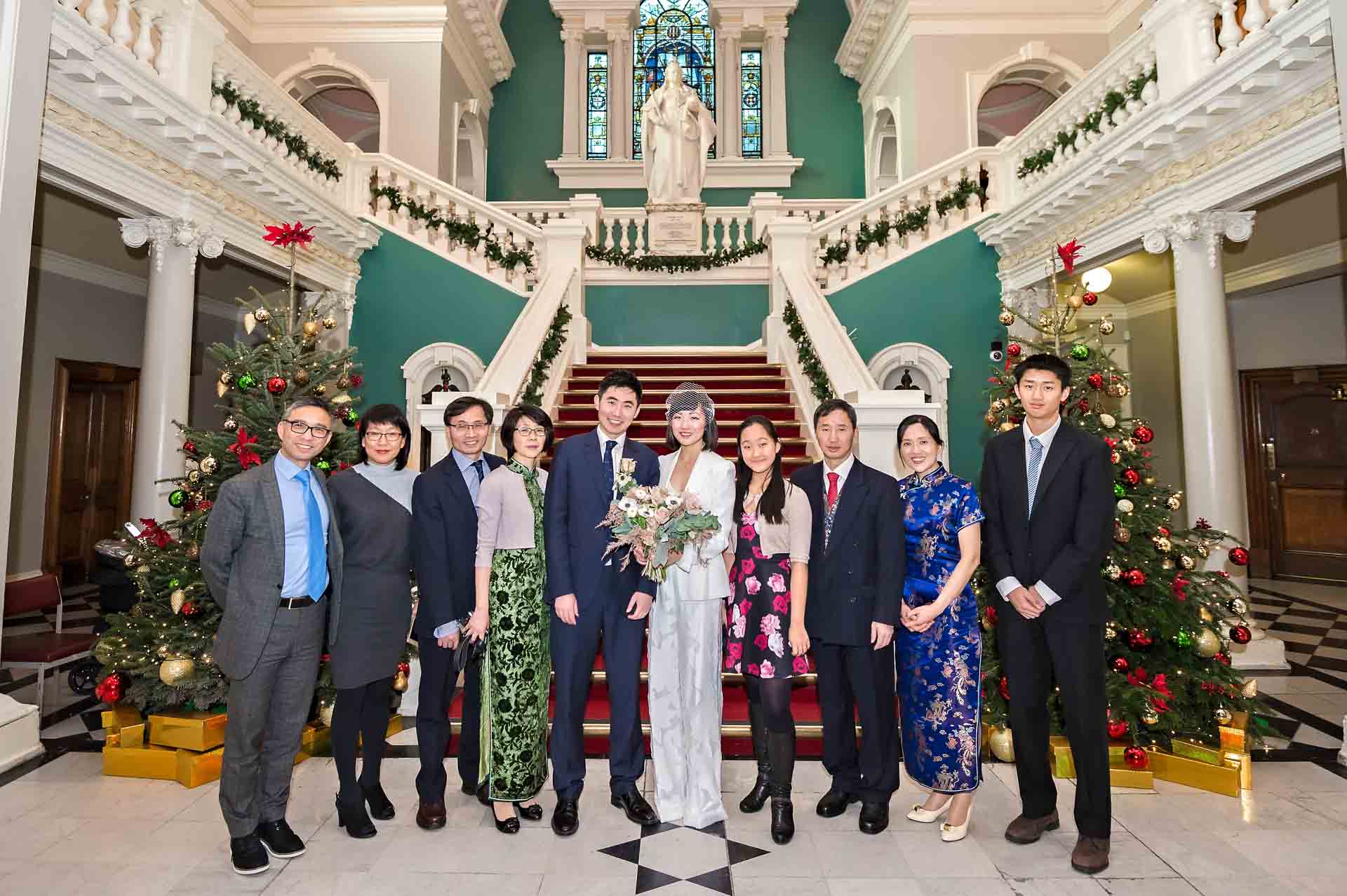 The entire wedding party pose in-front of the staircase in the Victorian Hall of Woolwich Town Hall