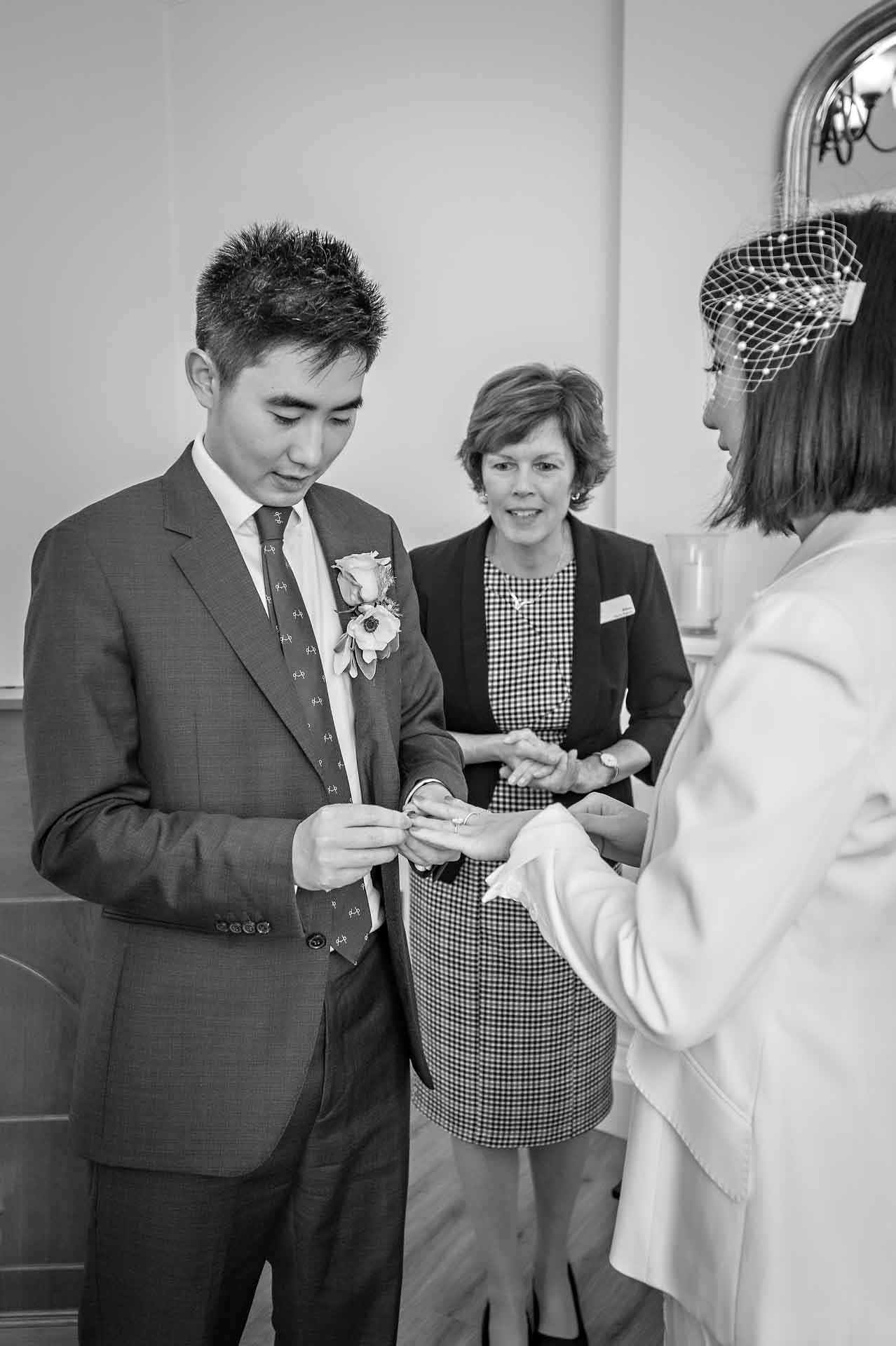 The groom places the ring on the bride's finger in the Edwardian Room at Woolwich Town Hall