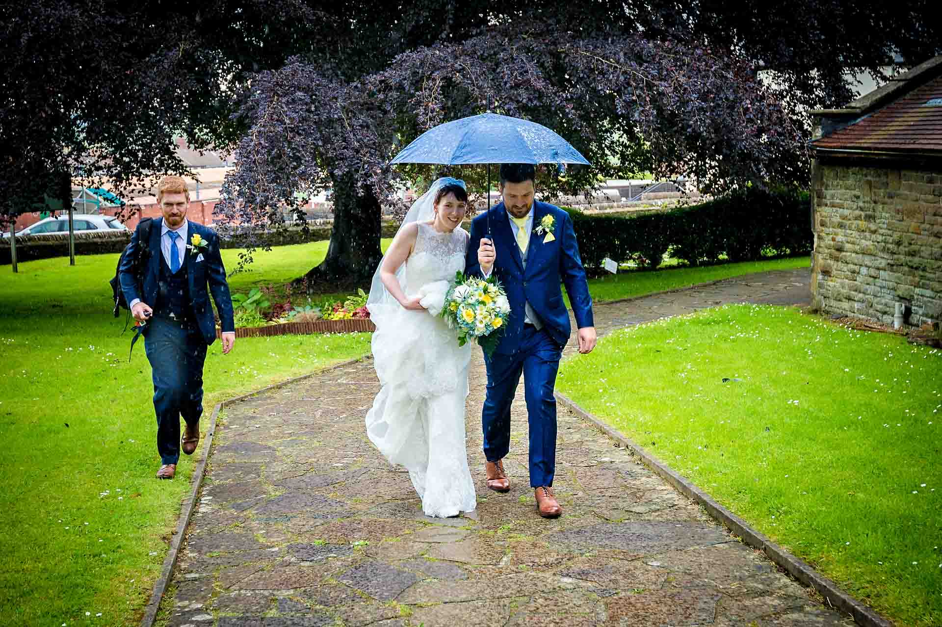 Couple walking along path with umbrella and friend walking behind