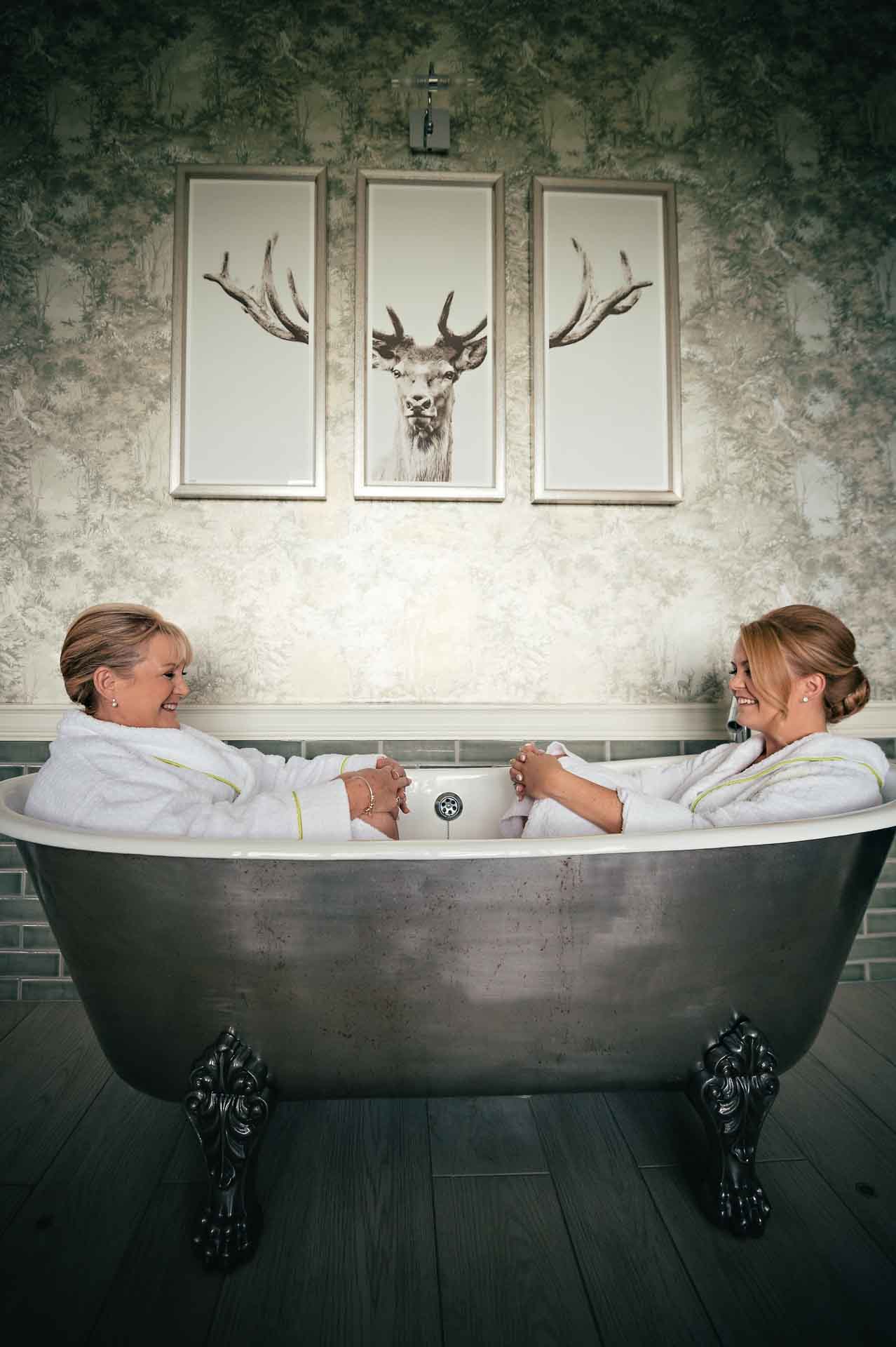 Bride with mother sitting in bath under portrait of deer