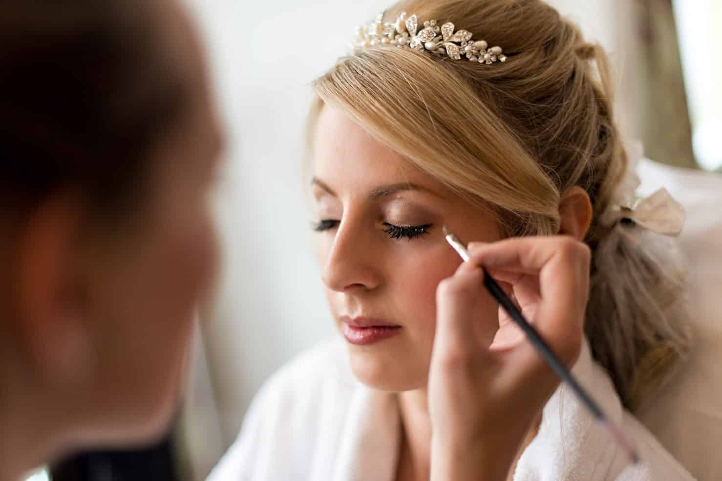 Bride with eyes shut having eyeliner applied by the make up artist