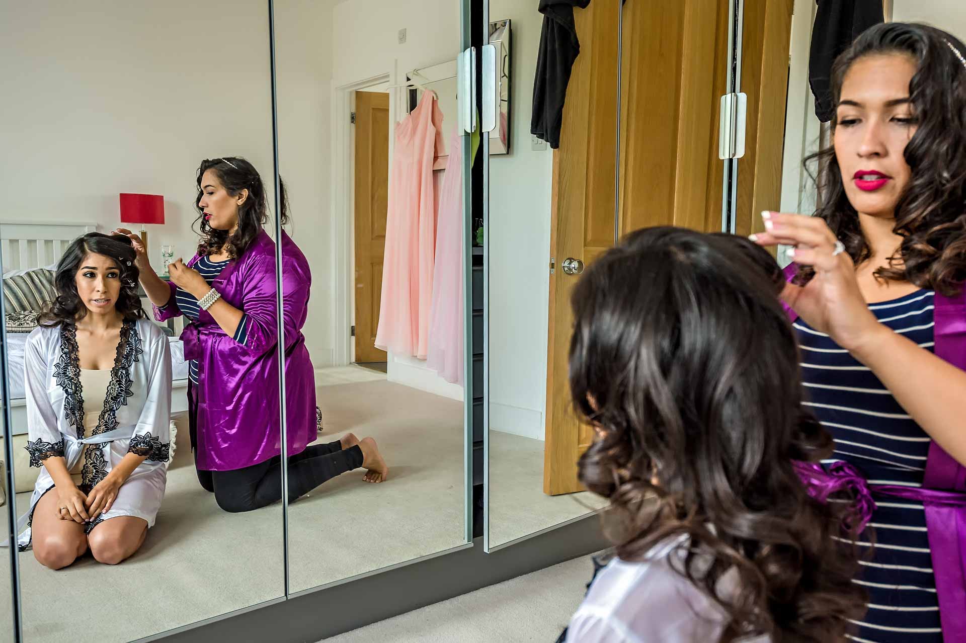 Bride in dressing gown having make up done in large wardrobe mirror