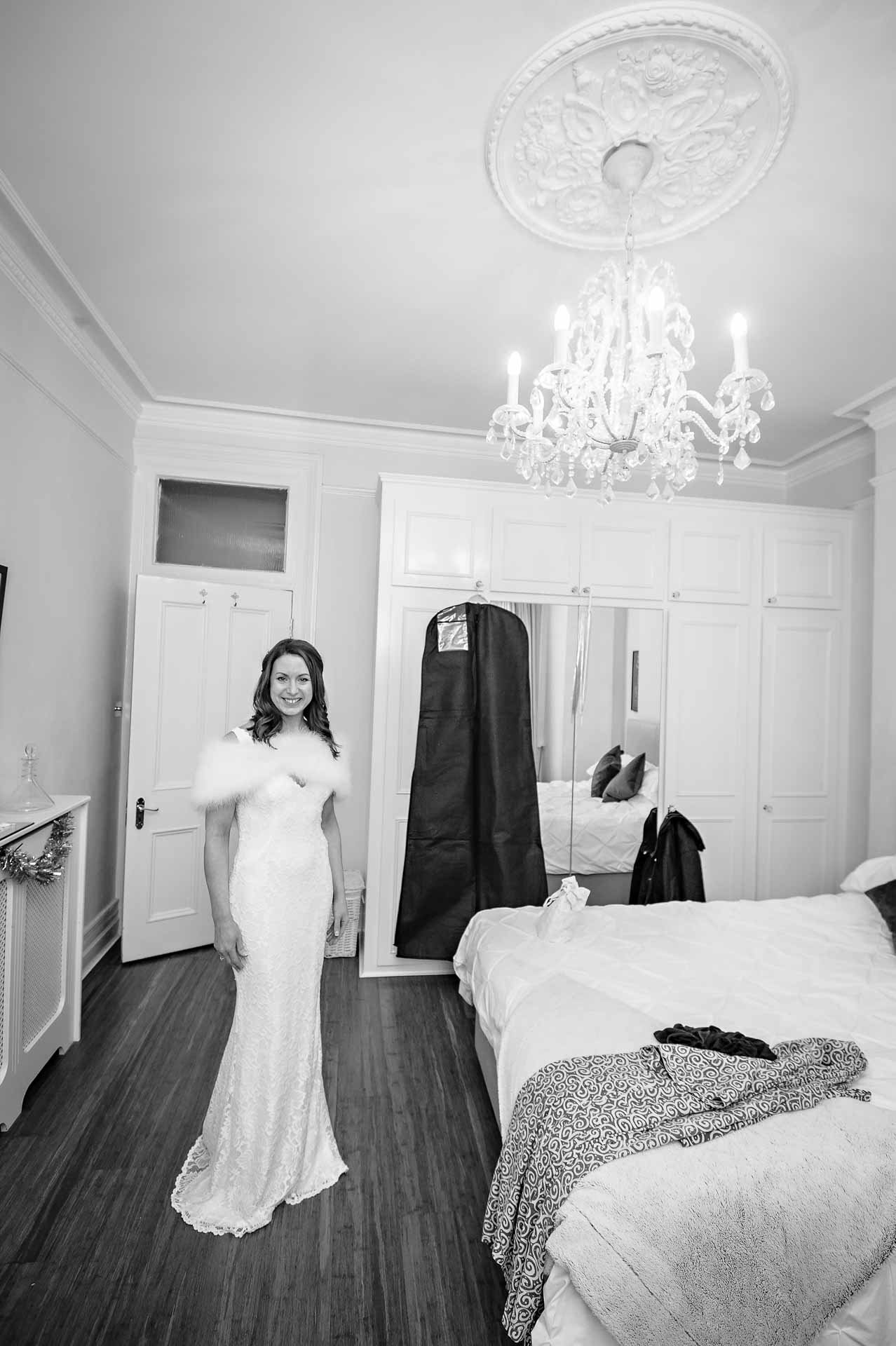 Black and white portrait of bride in room with clothes behind her and on bed