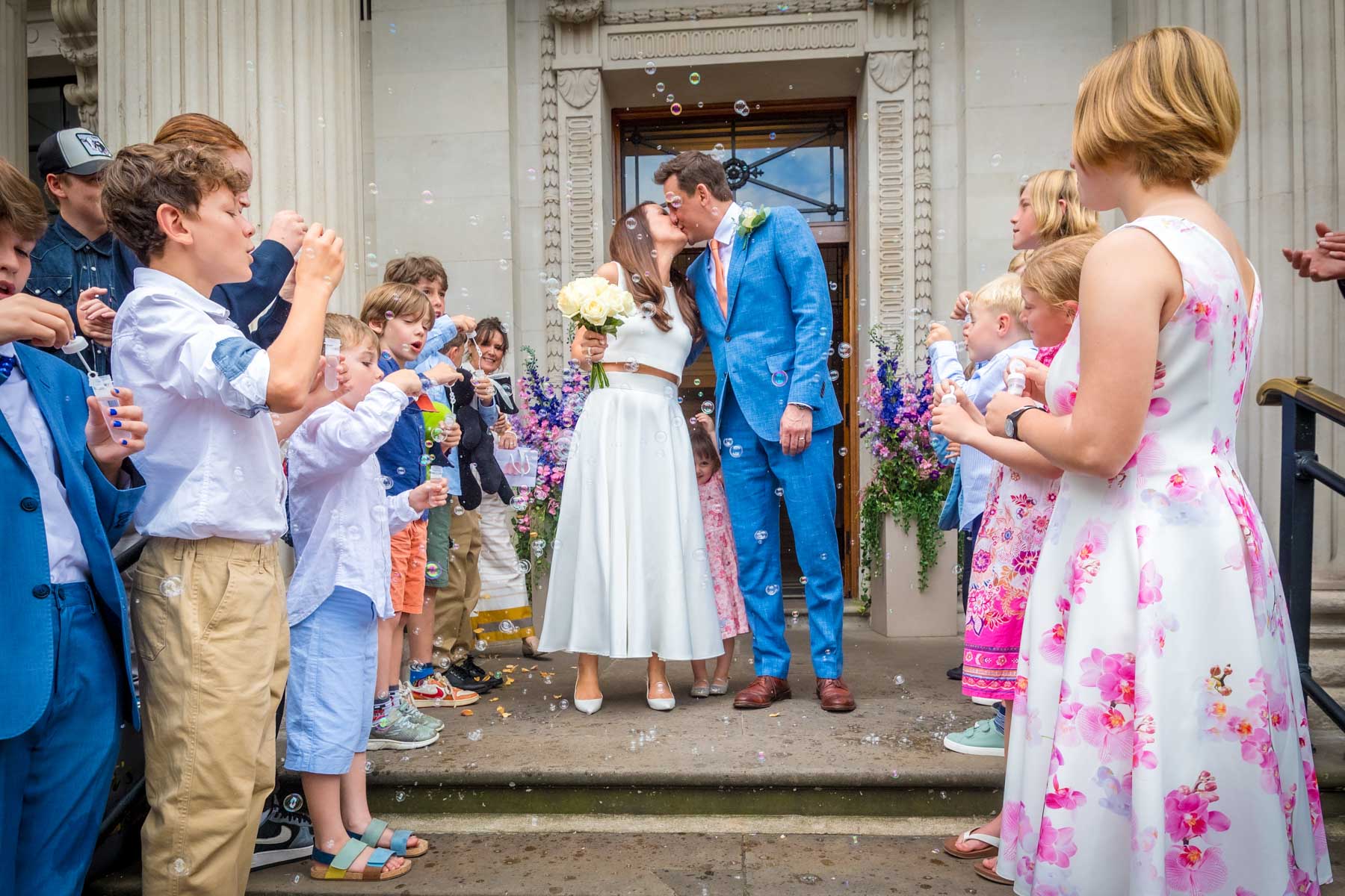 Couple kissing as guests blow bubbles at wedding outside Old Marylebone Town Hall