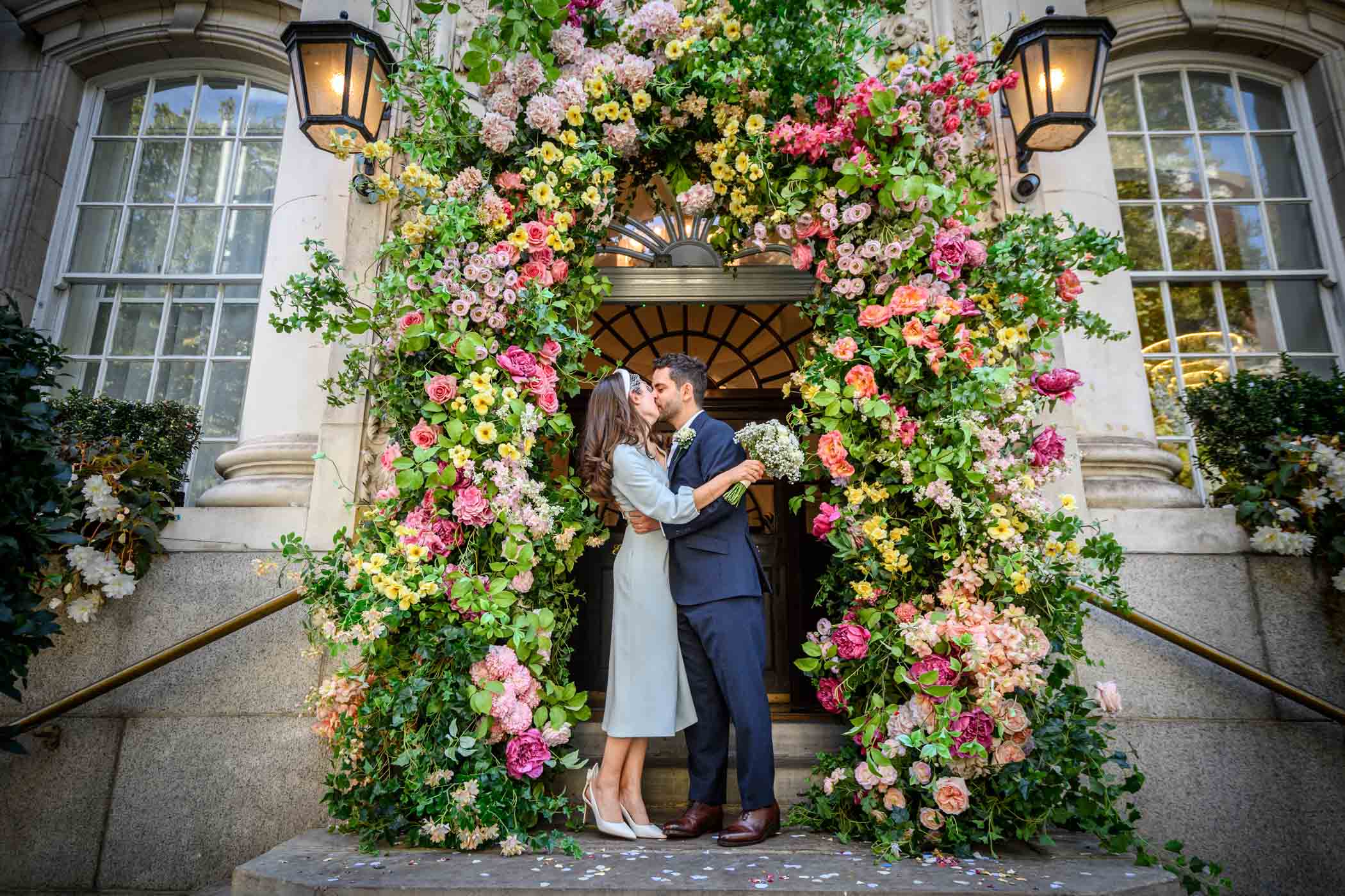 Couple kissing on steps of Chelsea Old Town Hall with floral display behind them