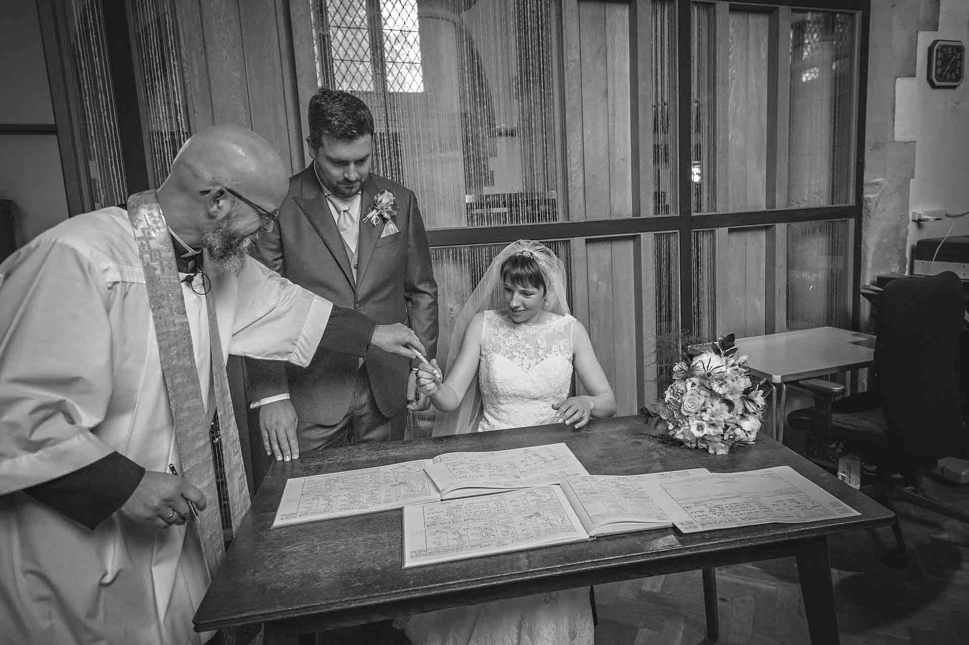 Vicar passing pen to bride to sign the church wedding register