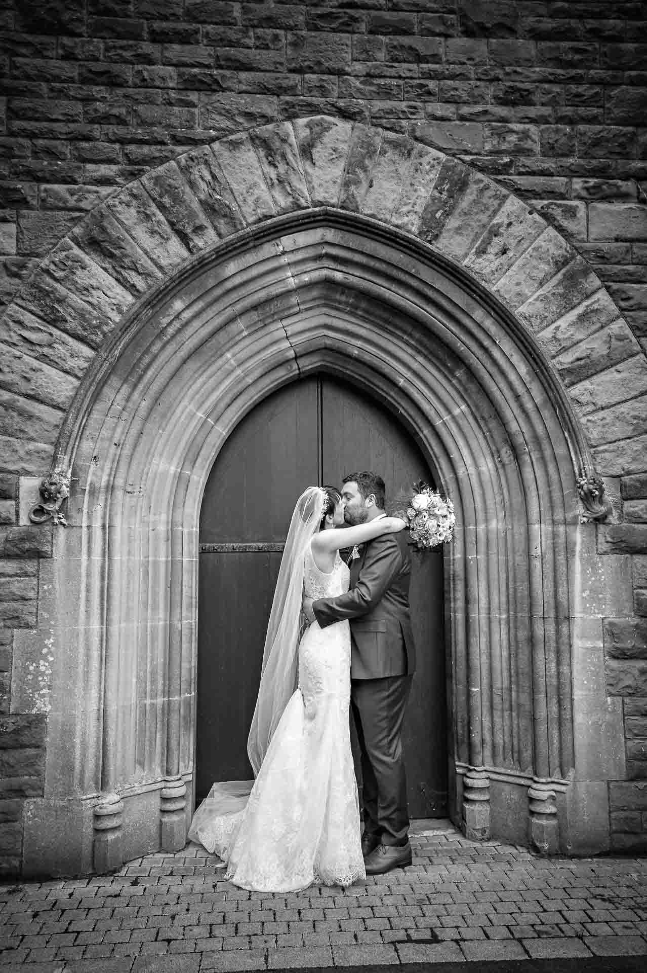 Couple kissing outside Gothic church door in South Wales